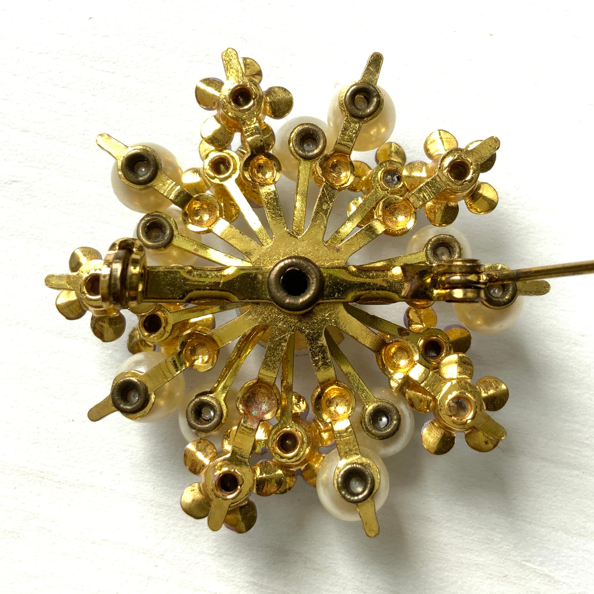 A brooch centered around large lilac-colored aurora borealis, adorned with small lilac enamel flowers and glass pearls. 大粒のライラックカラーのオーロラストーンを中心に、ライラックカラーのエナメルの小花とグラスパールがあしらわれたブローチ。