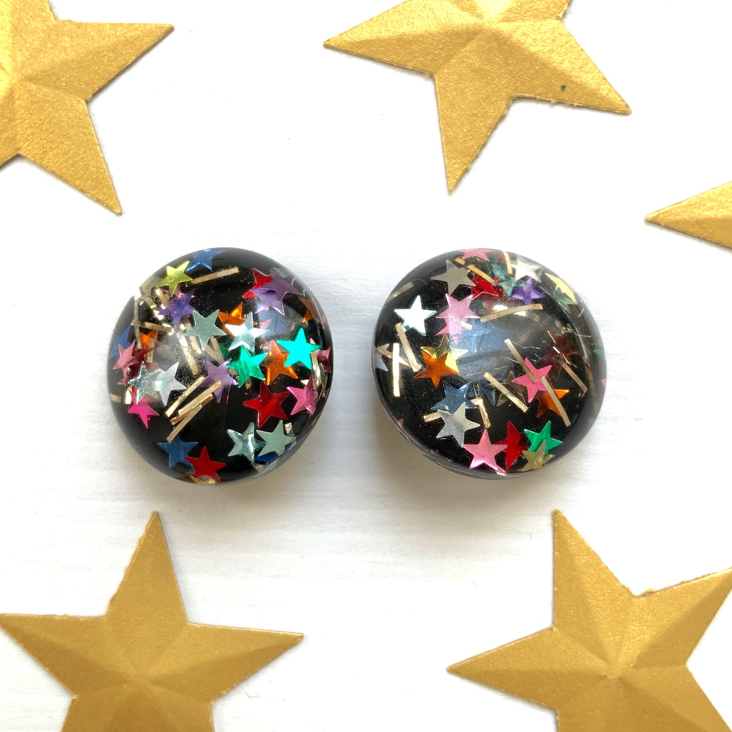 Clip-on earrings featuring a dome of black plastic filled with colourful star-shaped confetti. カラフルな星型コンフェッティが閉じ込められた、プラスチックドームのクリップイヤリング。