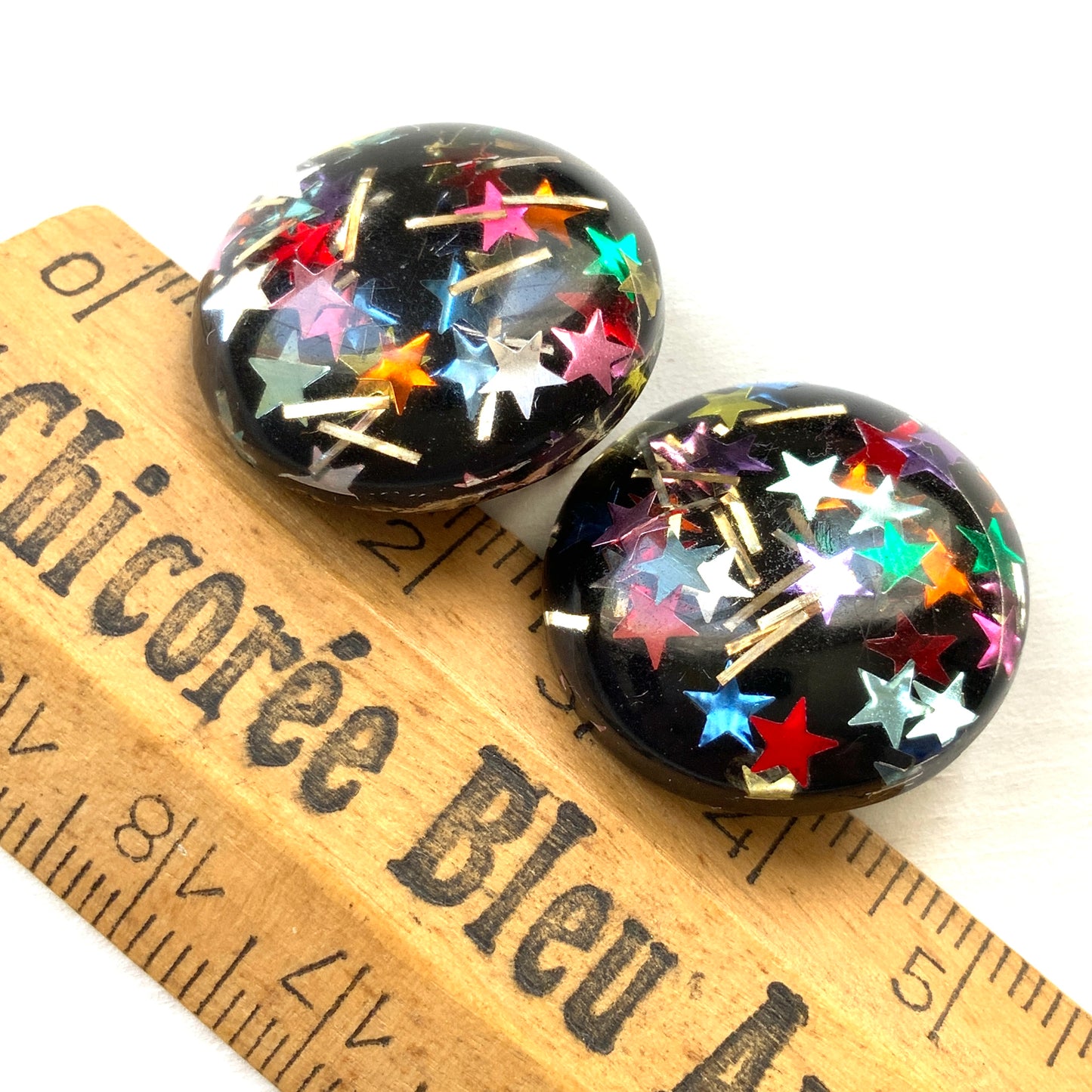 Clip-on earrings featuring a dome of black plastic filled with colourful star-shaped confetti. カラフルな星型コンフェッティが閉じ込められた、プラスチックドームのクリップイヤリング。