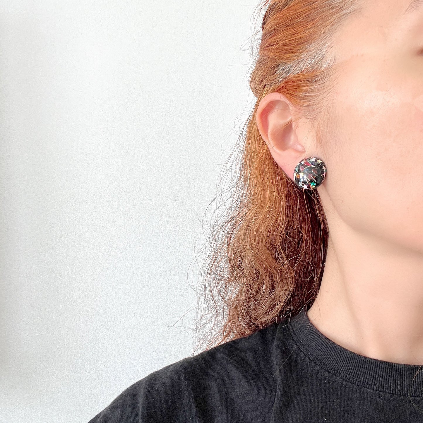 Clip-on earrings featuring a dome of black plastic filled with colourful star-shaped confetti. カラフルな星型コンフェッティが閉じ込められた、プラスチックドームのクリップイヤリング。