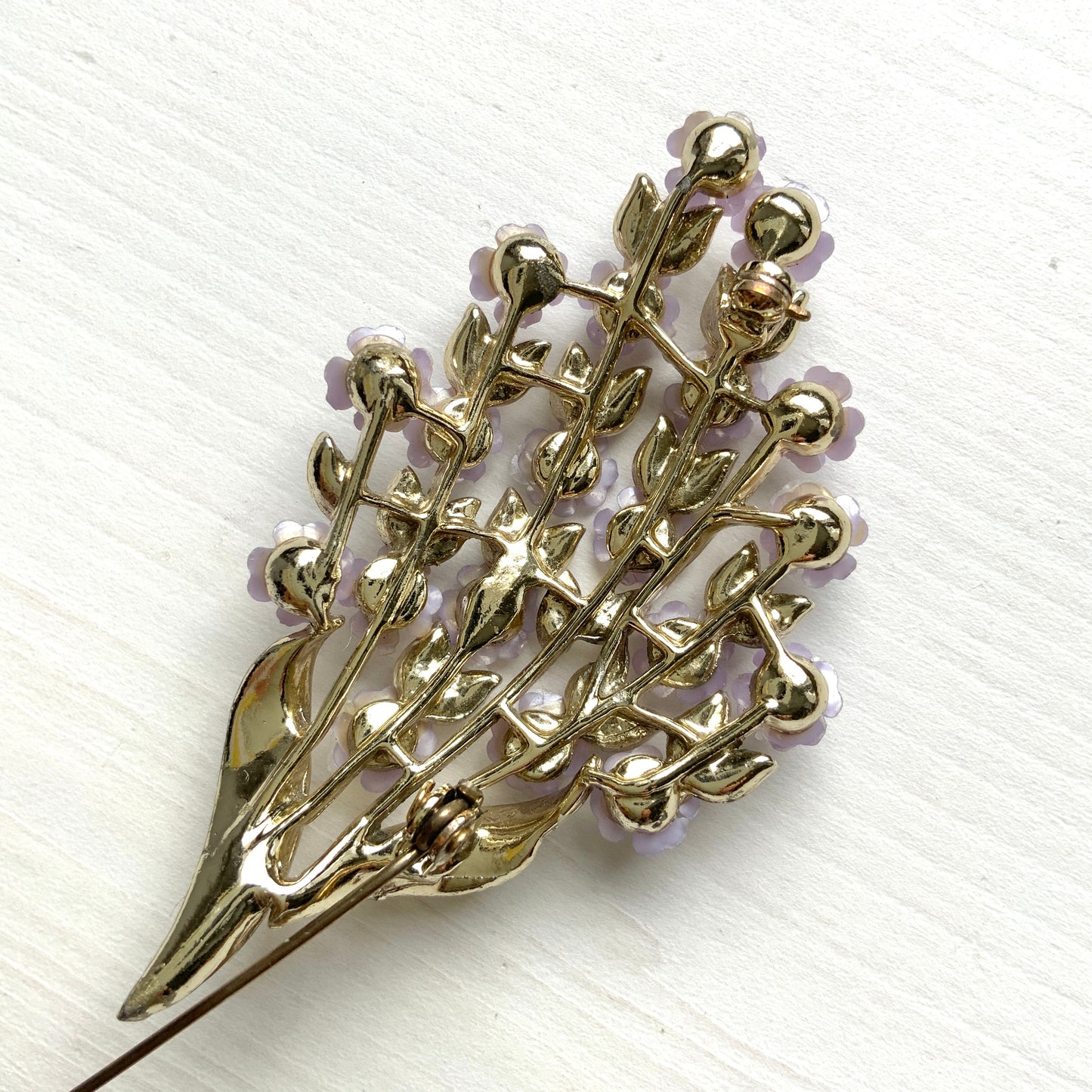 A brooch featuring charming light purple flowers resting on white enameled leaves. 白いエナメルの葉っぱにかわいらしい薄紫の小さなお花がたくさんついたブローチ。