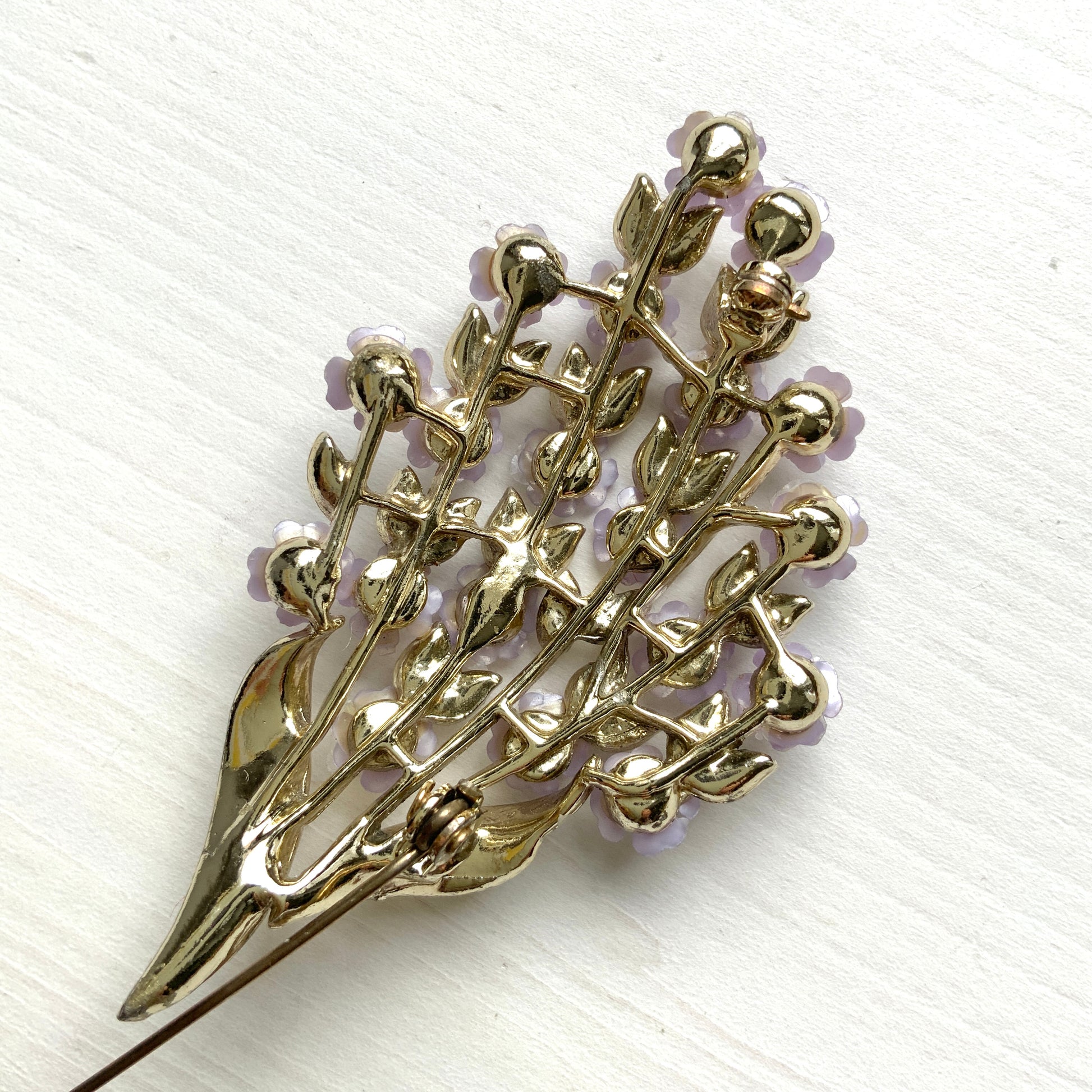 A brooch featuring charming light purple flowers resting on white enameled leaves. 白いエナメルの葉っぱにかわいらしい薄紫の小さなお花がたくさんついたブローチ。