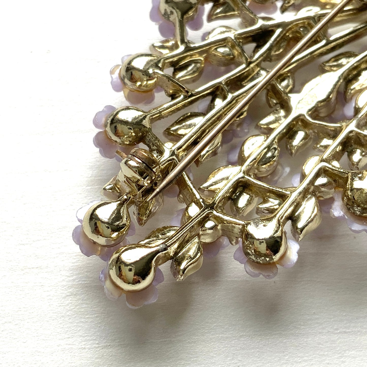 A brooch featuring charming light purple flowers resting on white enameled leaves. 白いエナメルの葉っぱにかわいらしい薄紫の小さなお花がたくさんついたブローチ。