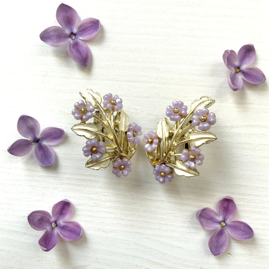 Charming clip-on earrings with pale purple blossoms adorning white enameled leaves. 白いエナメルの葉っぱに、かわいらしい薄紫のお花が咲いたクリップイヤリング。