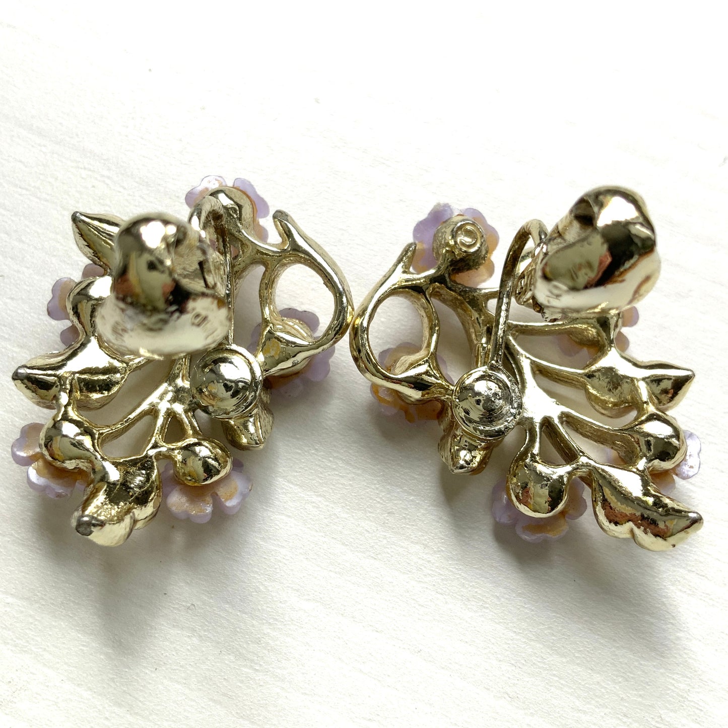 Charming clip-on earrings with pale purple blossoms adorning white enameled leaves. 白いエナメルの葉っぱに、かわいらしい薄紫のお花が咲いたクリップイヤリング。