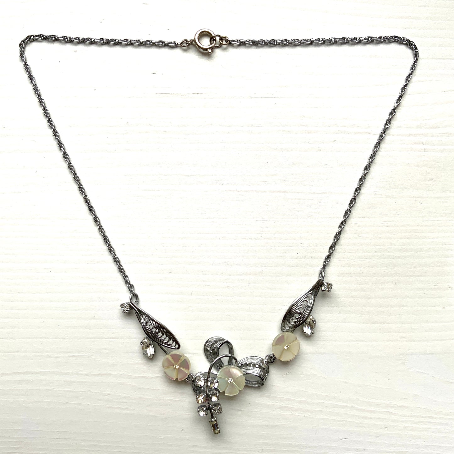 A charming necklace featuring tiny mother of pearl flowers, silver-tone filigree leaves, and clear rhinestone accents. かわいらしいマザーオブパールの小さなお花と、シルバートーンのフィリグリーやクリアラインストーン のリーフのネックレス。