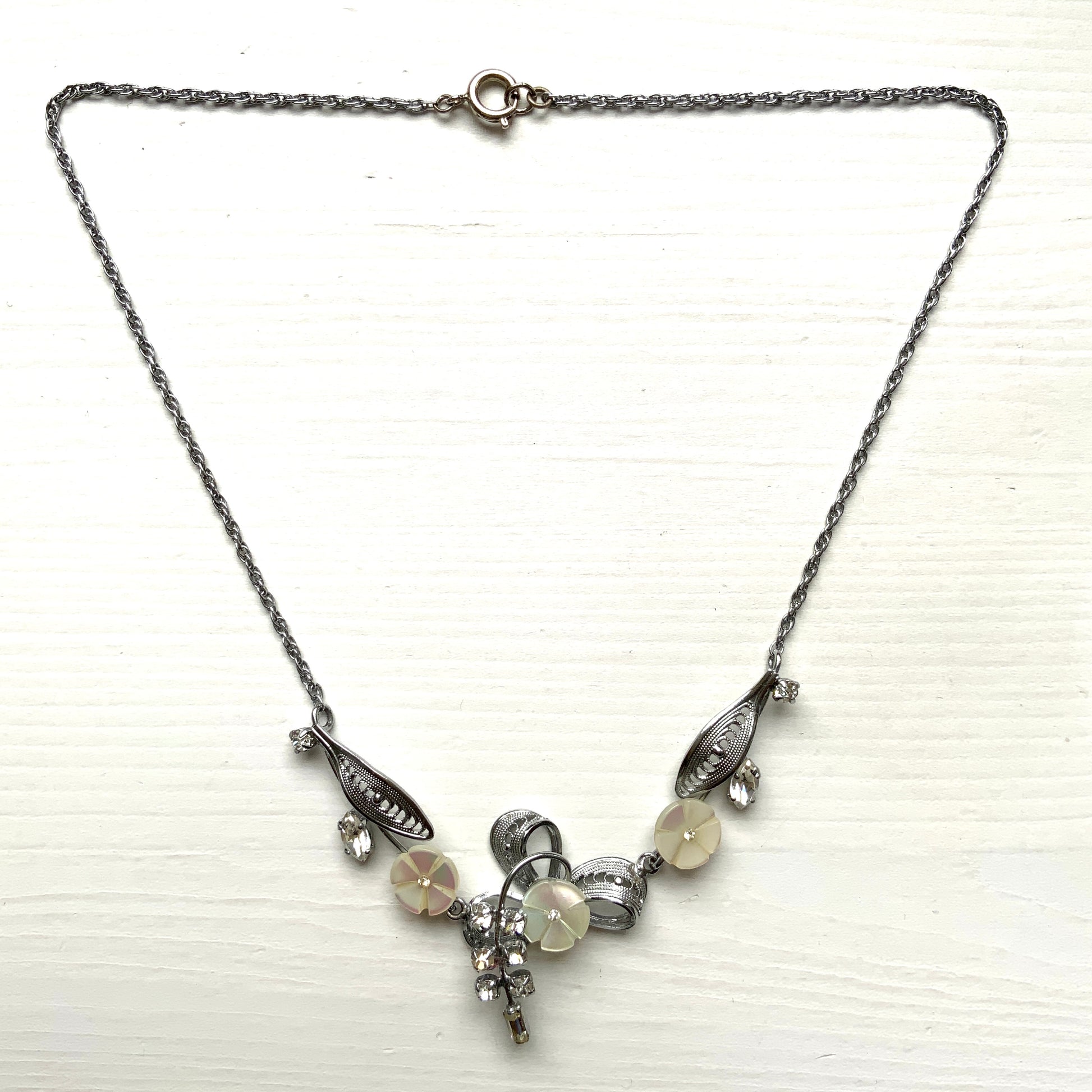 A charming necklace featuring tiny mother of pearl flowers, silver-tone filigree leaves, and clear rhinestone accents. かわいらしいマザーオブパールの小さなお花と、シルバートーンのフィリグリーやクリアラインストーン のリーフのネックレス。
