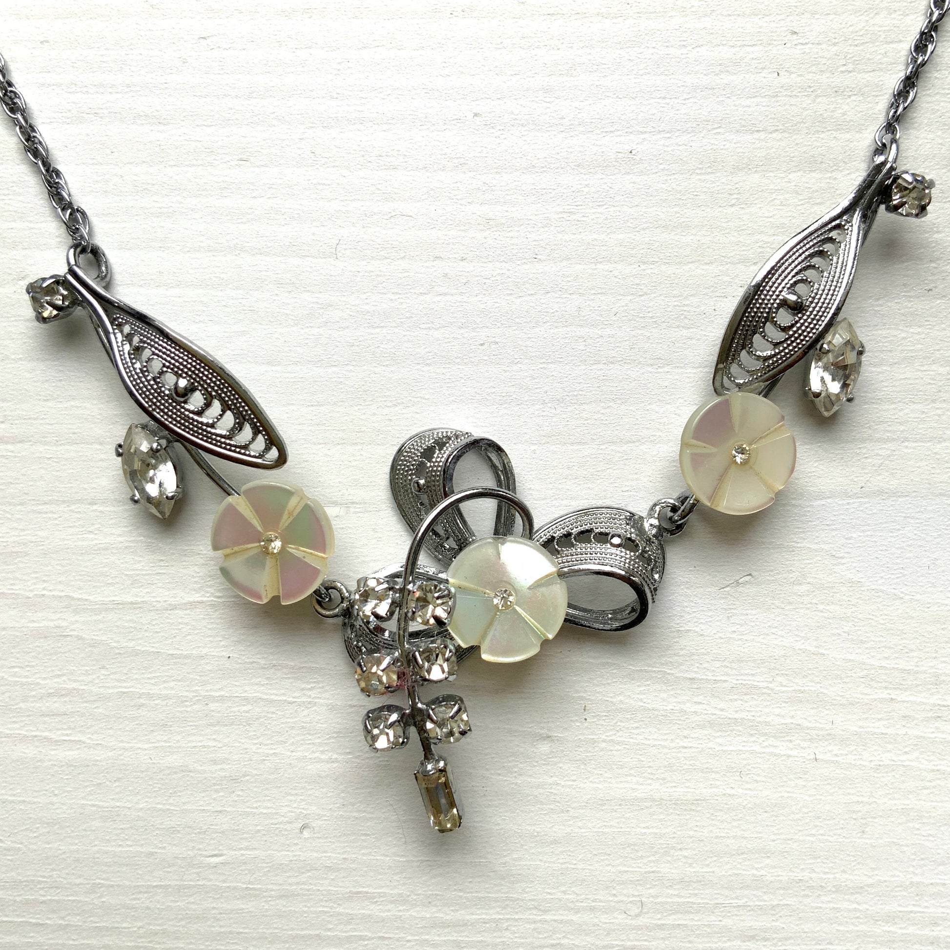A charming necklace featuring tiny mother of pearl flowers, silver-tone filigree leaves, and clear rhinestone accents. かわいらしいマザーオブパールの小さなお花と、シルバートーンのフィリグリーやクリアラインストーン のリーフのネックレス。