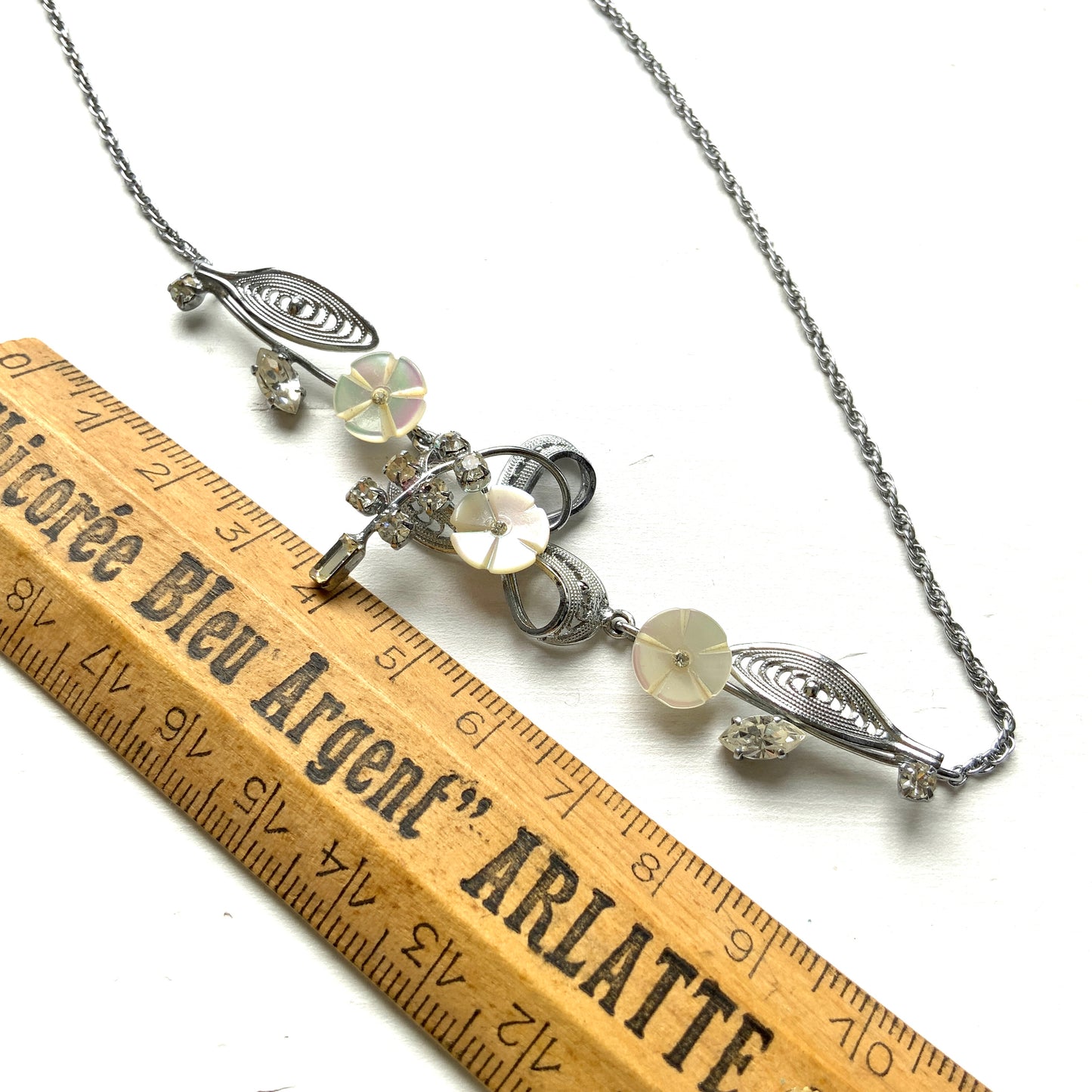 A charming necklace featuring tiny mother of pearl flowers, silver-tone filigree leaves, and clear rhinestone accents. かわいらしいマザーオブパールの小さなお花と、シルバートーンのフィリグリーやクリアラインストーン のリーフのネックレス。