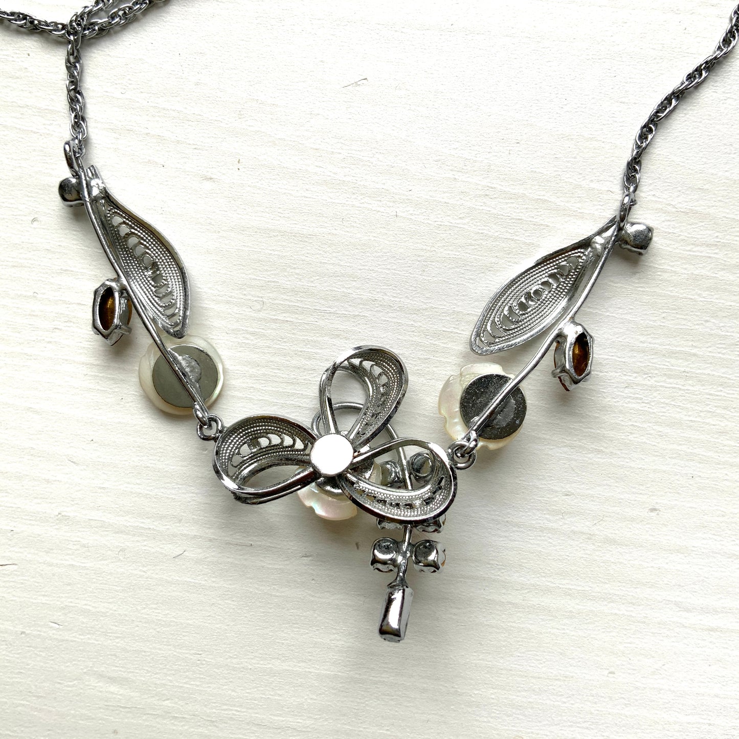 A charming necklace featuring tiny mother of pearl flowers, silver-tone filigree leaves, and clear rhinestone accents. かわいらしいマザーオブパールの小さなお花と、シルバートーンのフィリグリーやクリアラインストーン のリーフのネックレス。