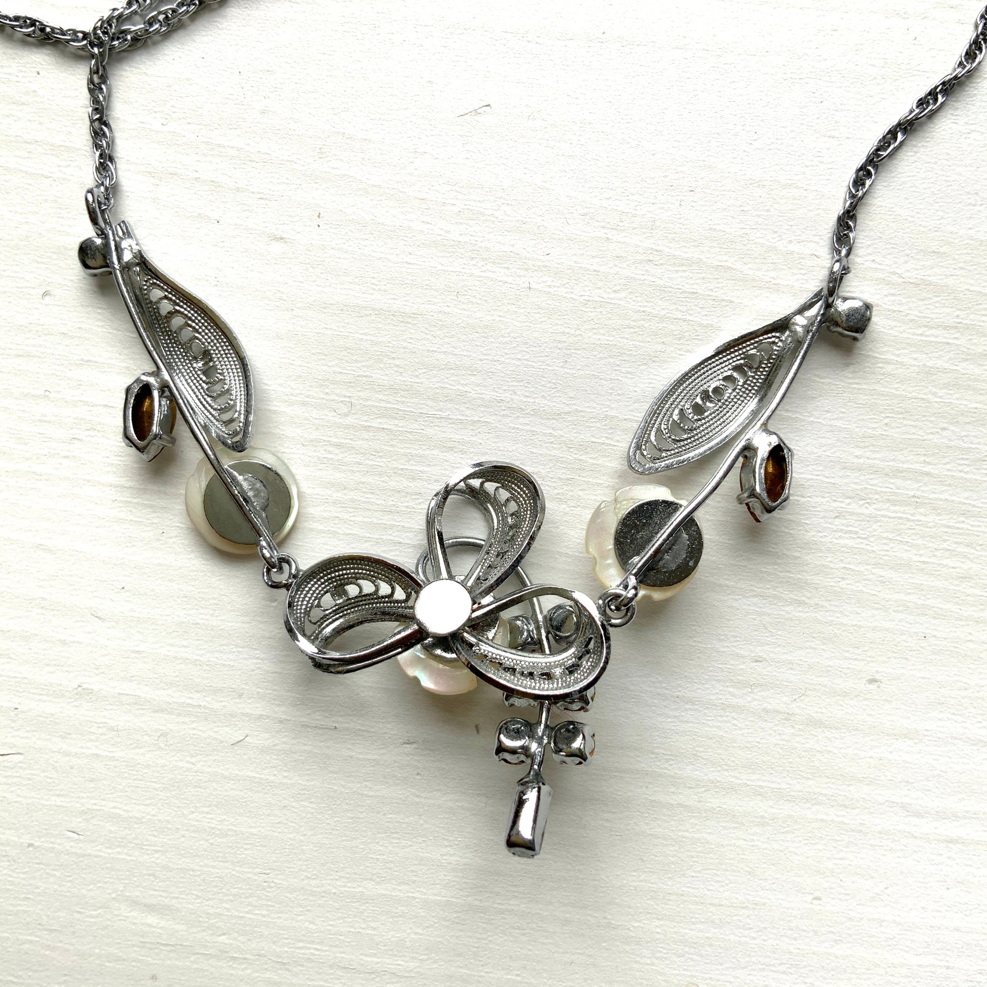 A charming necklace featuring tiny mother of pearl flowers, silver-tone filigree leaves, and clear rhinestone accents. かわいらしいマザーオブパールの小さなお花と、シルバートーンのフィリグリーやクリアラインストーン のリーフのネックレス。