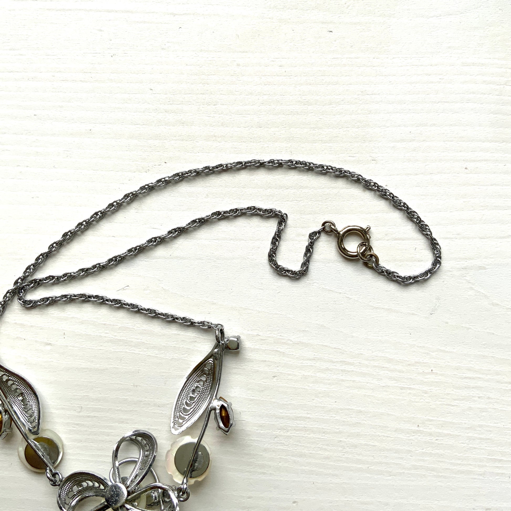 A charming necklace featuring tiny mother of pearl flowers, silver-tone filigree leaves, and clear rhinestone accents. かわいらしいマザーオブパールの小さなお花と、シルバートーンのフィリグリーやクリアラインストーン のリーフのネックレス。