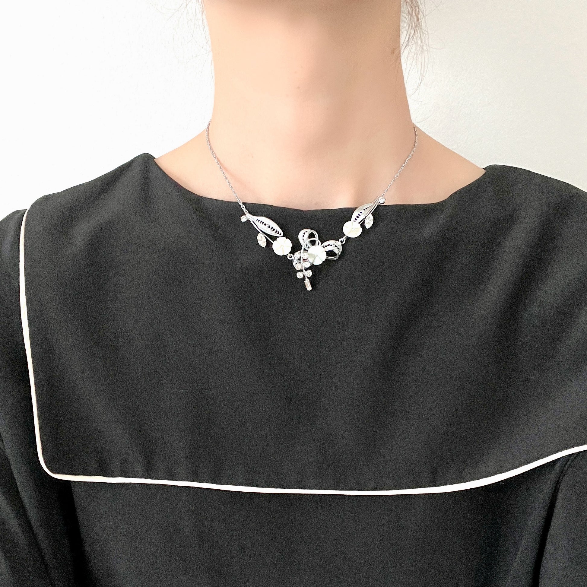 A charming necklace featuring tiny mother of pearl flowers, silver-tone filigree leaves, and clear rhinestone accents. かわいらしいマザーオブパールの小さなお花と、シルバートーンのフィリグリーやクリアラインストーン のリーフのネックレス。