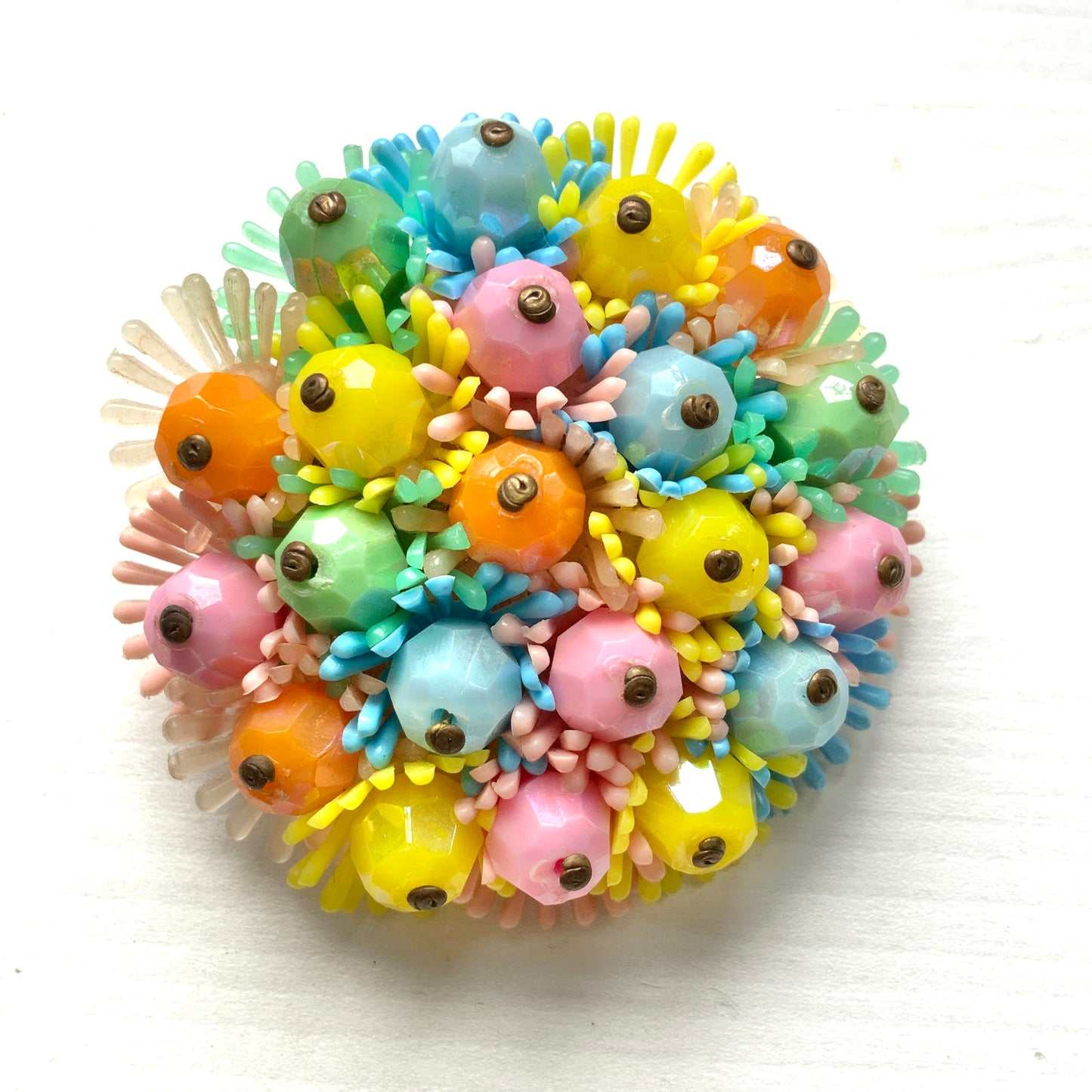 A round brooch featuring colourful candy-coloured soft plastic flowers. カラフルなキャンディーカラーのソフトプラスチックのお花が集まったラウンドブローチ。