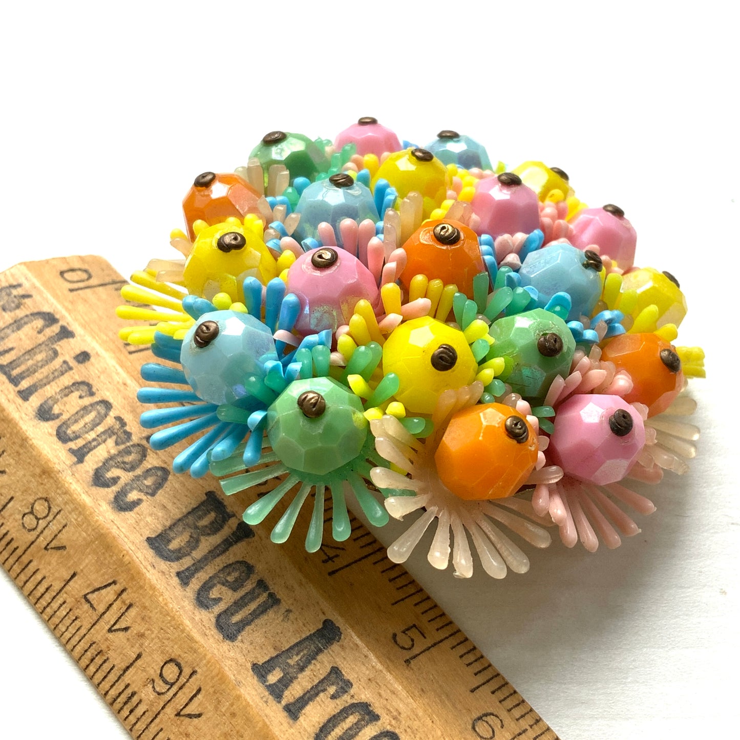 A round brooch featuring colourful candy-coloured soft plastic flowers. カラフルなキャンディーカラーのソフトプラスチックのお花が集まったラウンドブローチ。