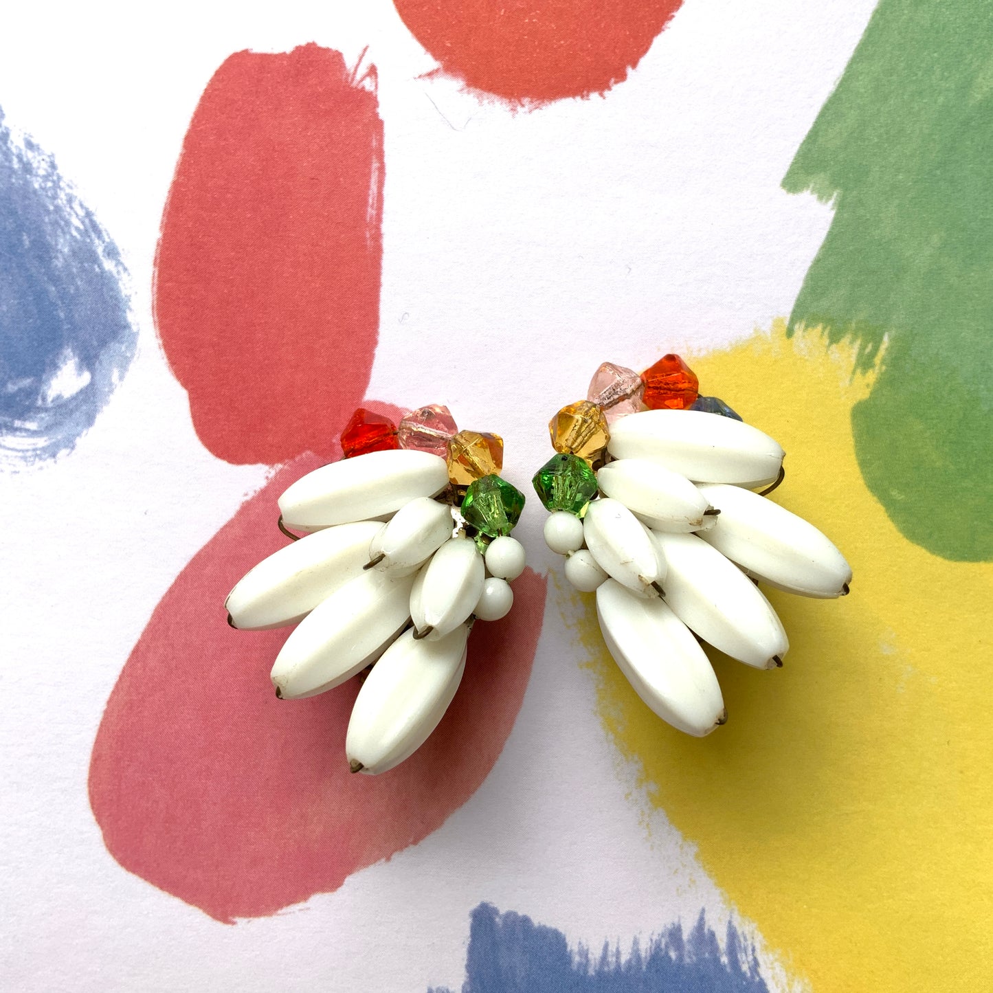 Clip-on earrings featuring layered white plastic beads arranged in a wing-like shape, accented with colourful faceted glass beads. 白い羽のようなロングプラスチックビーズに、カラフルなグラスビーズが彩りを添えたクリップイヤリング。