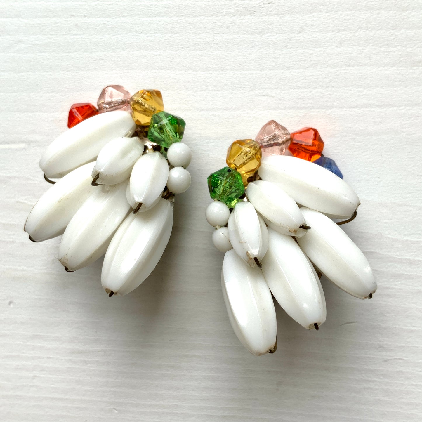 Clip-on earrings featuring layered white plastic beads arranged in a wing-like shape, accented with colourful faceted glass beads. 白い羽のようなロングプラスチックビーズに、カラフルなグラスビーズが彩りを添えたクリップイヤリング。