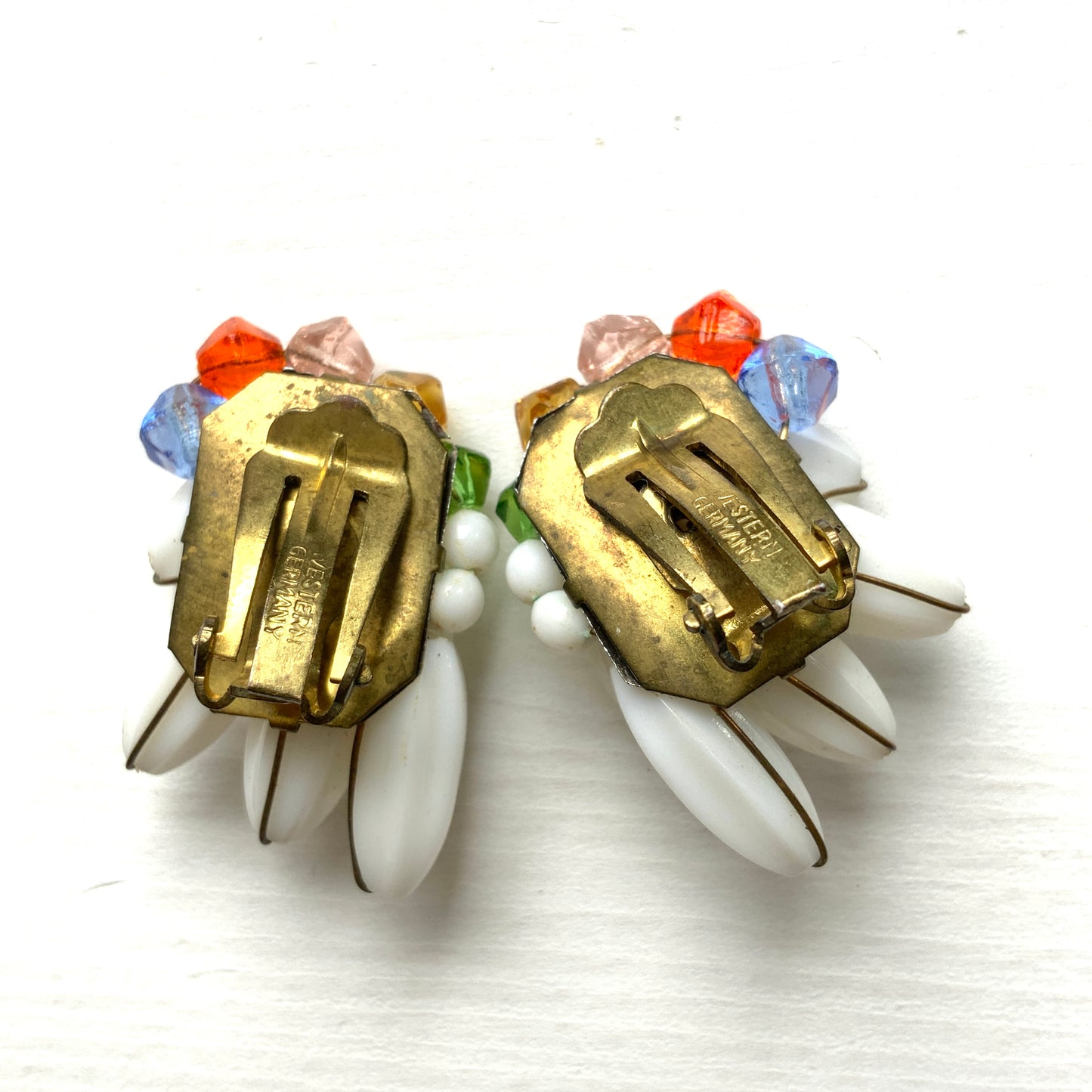 Clip-on earrings featuring layered white plastic beads arranged in a wing-like shape, accented with colourful faceted glass beads. 白い羽のようなロングプラスチックビーズに、カラフルなグラスビーズが彩りを添えたクリップイヤリング。