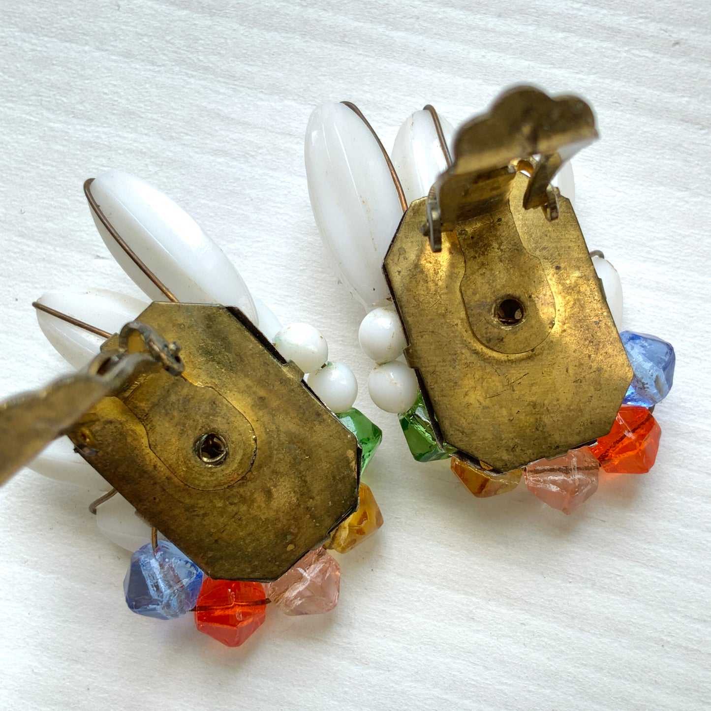 Clip-on earrings featuring layered white plastic beads arranged in a wing-like shape, accented with colourful faceted glass beads. 白い羽のようなロングプラスチックビーズに、カラフルなグラスビーズが彩りを添えたクリップイヤリング。