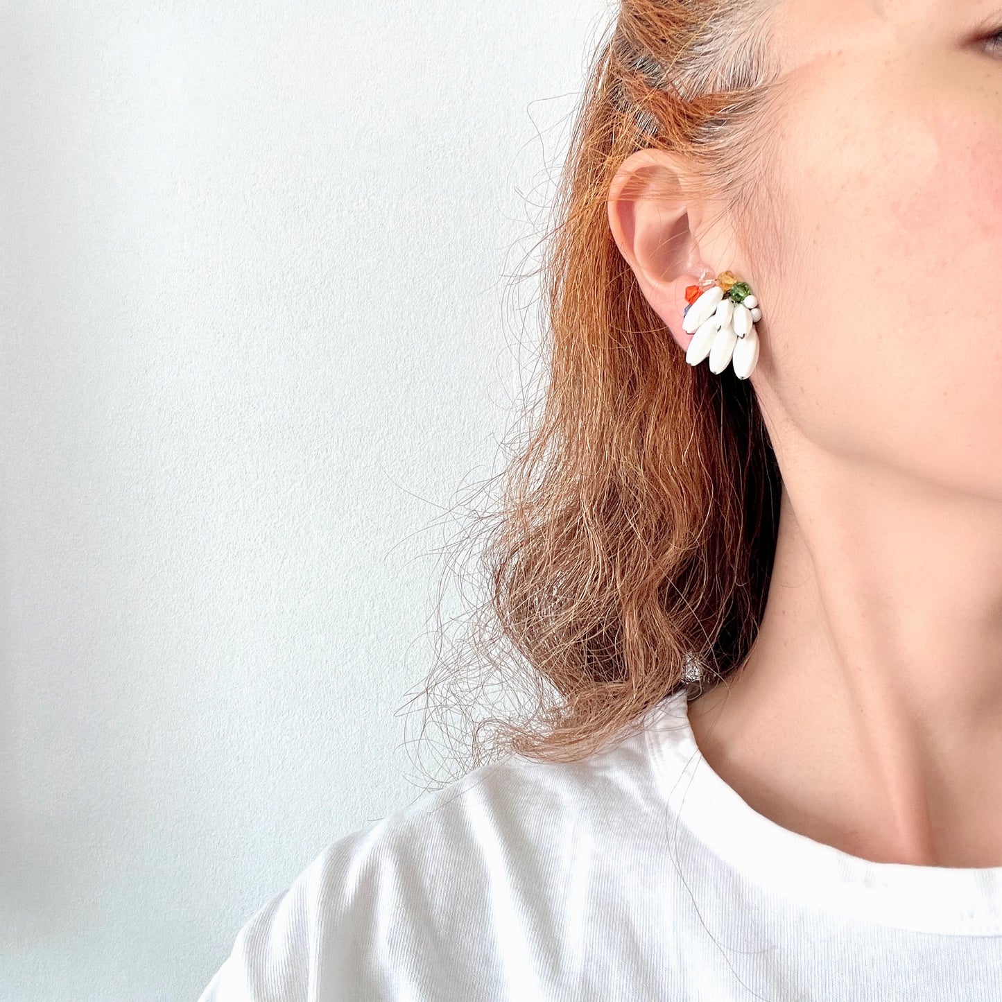Clip-on earrings featuring layered white plastic beads arranged in a wing-like shape, accented with colourful faceted glass beads. 白い羽のようなロングプラスチックビーズに、カラフルなグラスビーズが彩りを添えたクリップイヤリング。