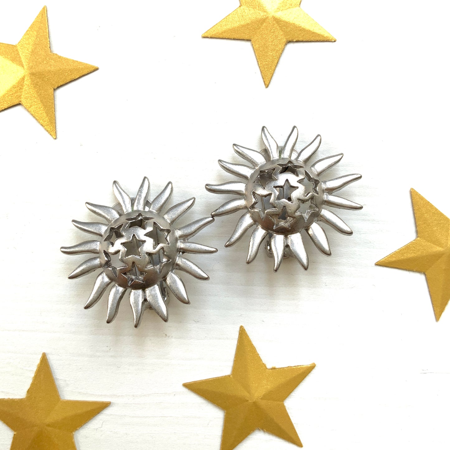 Clip-on earrings featuring a silver-tone sun motif with star-shaped cut-outs. シルバートーンの太陽モチーフに、星型のカットアウトが施されたクリップイヤリング。