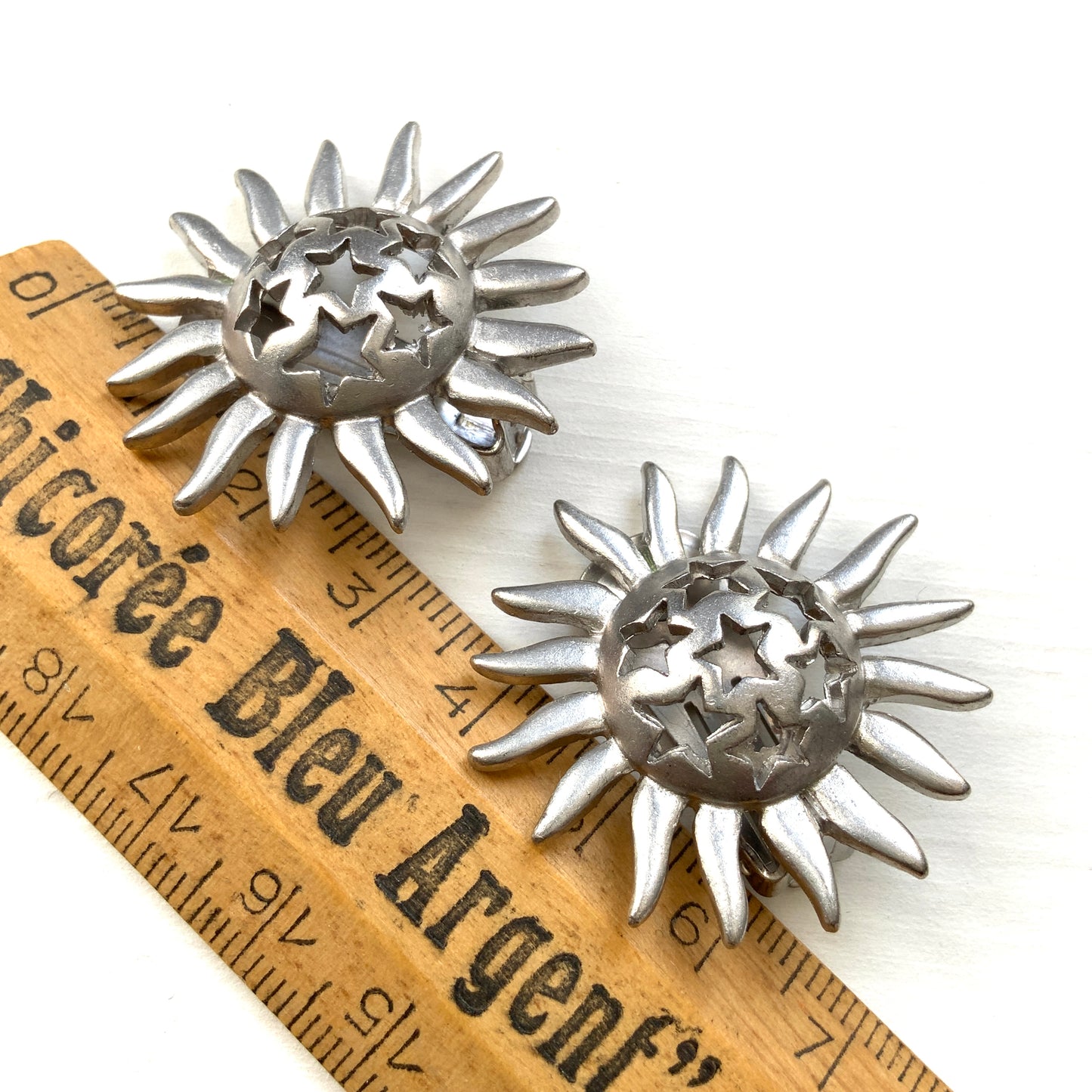 Clip-on earrings featuring a silver-tone sun motif with star-shaped cut-outs. シルバートーンの太陽モチーフに、星型のカットアウトが施されたクリップイヤリング。