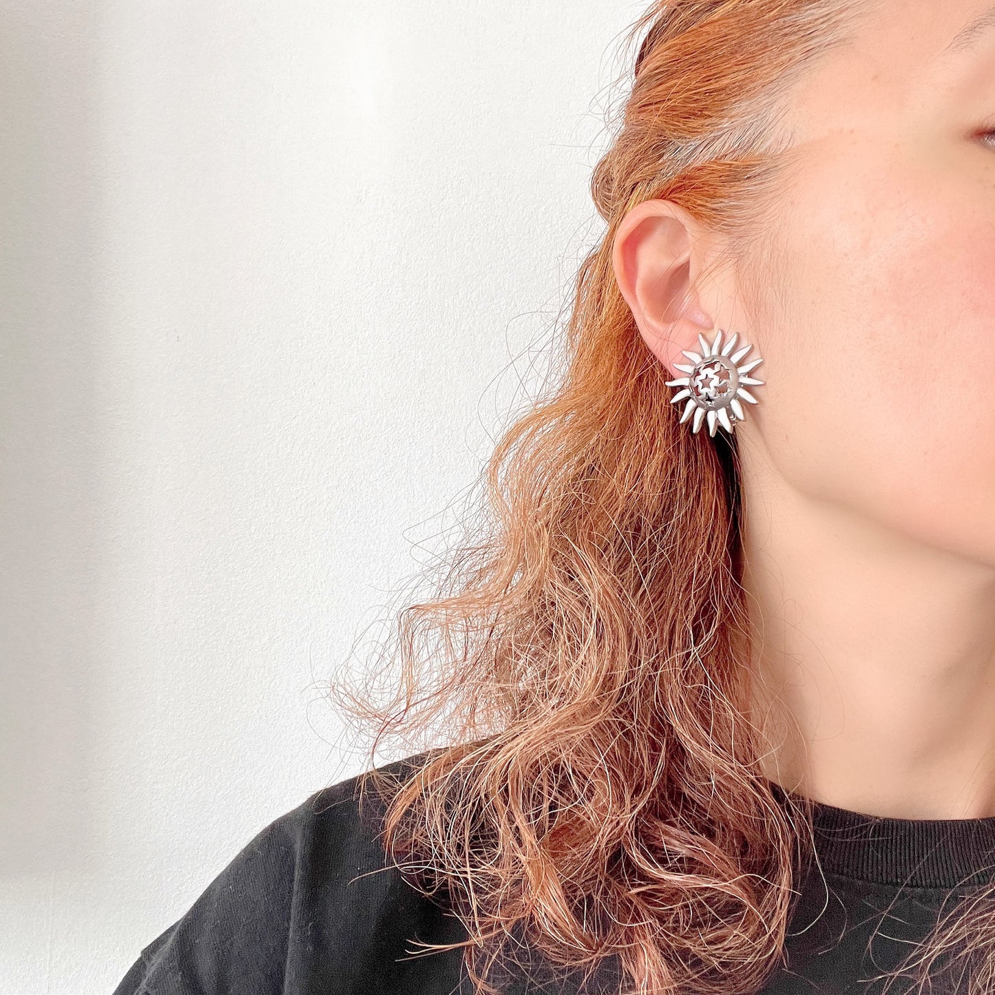 Clip-on earrings featuring a silver-tone sun motif with star-shaped cut-outs. シルバートーンの太陽モチーフに、星型のカットアウトが施されたクリップイヤリング。