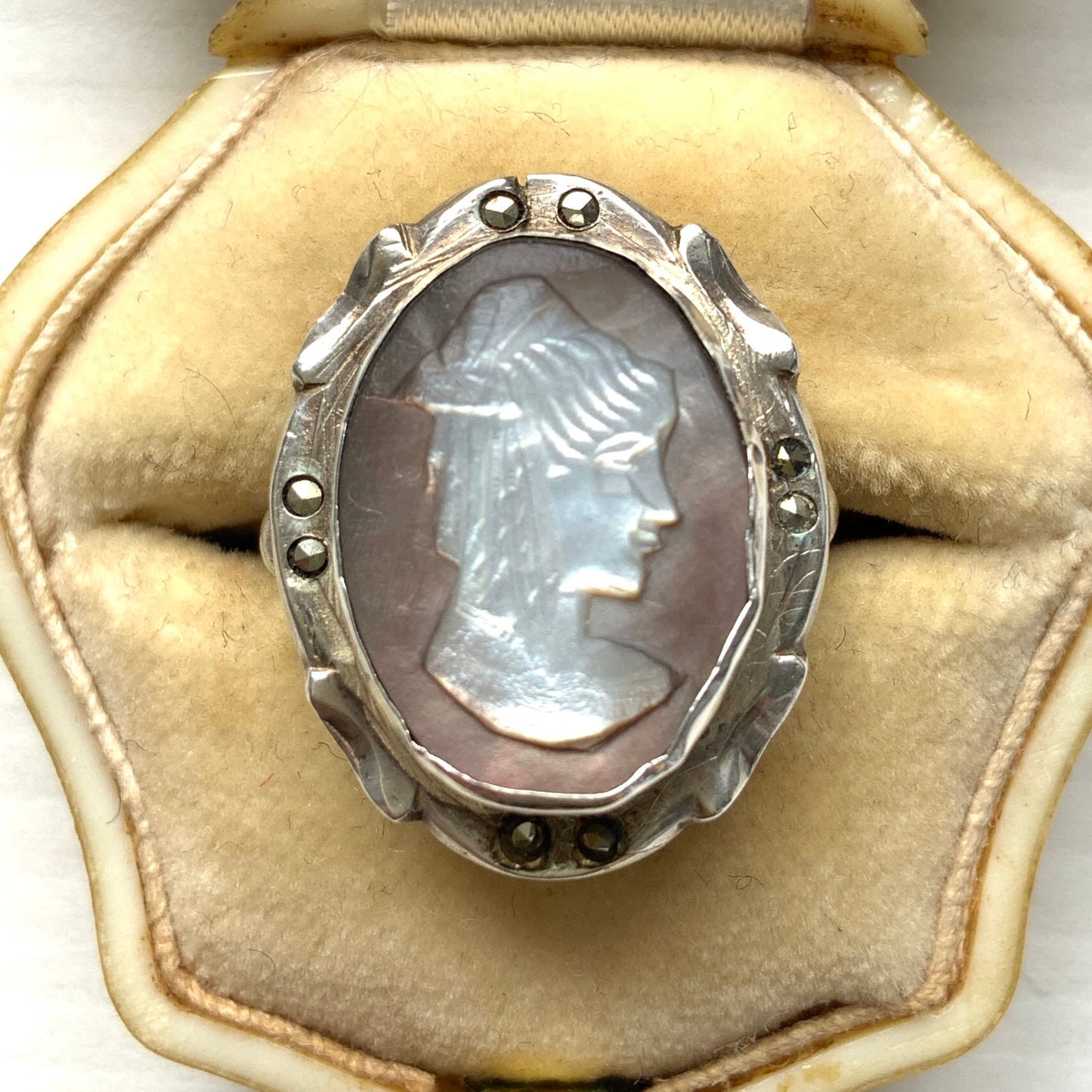 A silver ring with a cameo carved from mother of pearl, featuring the white layer carved into the profile of a lady against an iridescent grey-pink background. 白蝶貝(マザーオブパール)の白い層を彫り出し、グレー〜ピンクがかった虹色の層を背景にしたカメオのシルバーリング。