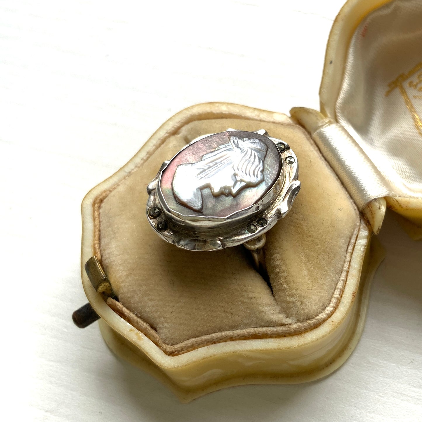 A silver ring with a cameo carved from mother of pearl, featuring the white layer carved into the profile of a lady against an iridescent grey-pink background. 白蝶貝(マザーオブパール)の白い層を彫り出し、グレー〜ピンクがかった虹色の層を背景にしたカメオのシルバーリング。