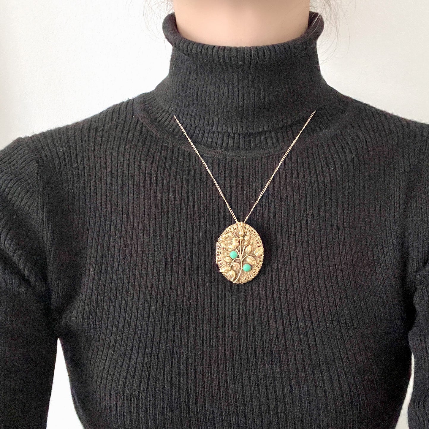 A gold-tone locket brooch featuring a floral motif accented with turquoise blue cabochons. ゴールドトーンのお花に、ターコイズブルーのカボションが映えるロケットブローチ。