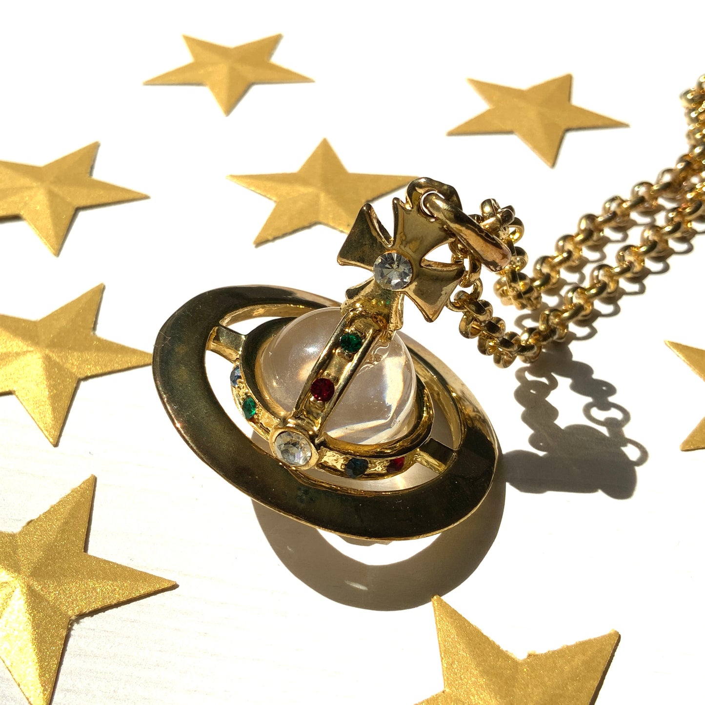 A striking pendant necklace featuring a decorative orb encircled by a metal hoop, resembling the rings of Saturn. カラフルなストーンで飾られた宝珠(キリスト教圏で、十字架をのせた球体として王権の象徴に用いられるモチーフ)を、まるで土星の輪のようなメタルフープで囲んだデザインのペンダントネックレスです。