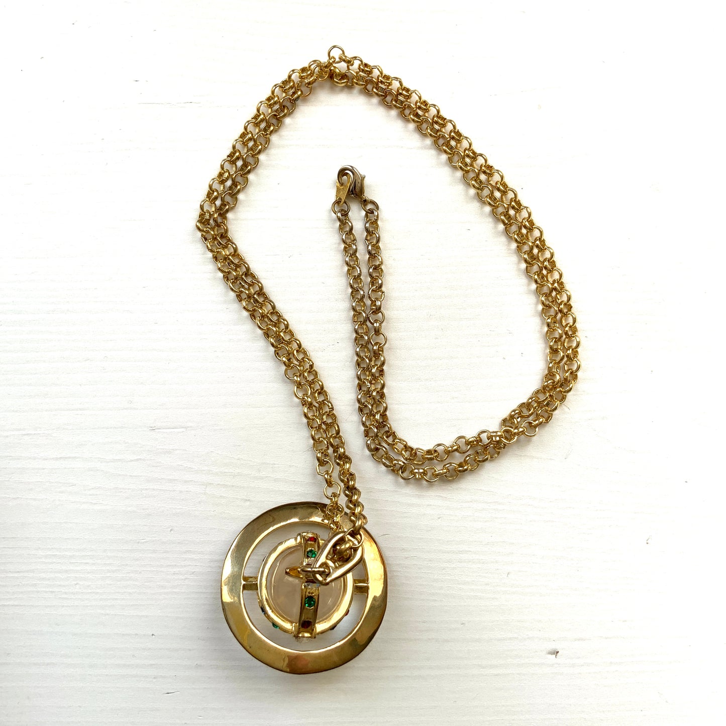 A striking pendant necklace featuring a decorative orb encircled by a metal hoop, resembling the rings of Saturn. カラフルなストーンで飾られた宝珠(キリスト教圏で、十字架をのせた球体として王権の象徴に用いられるモチーフ)を、まるで土星の輪のようなメタルフープで囲んだデザインのペンダントネックレスです。