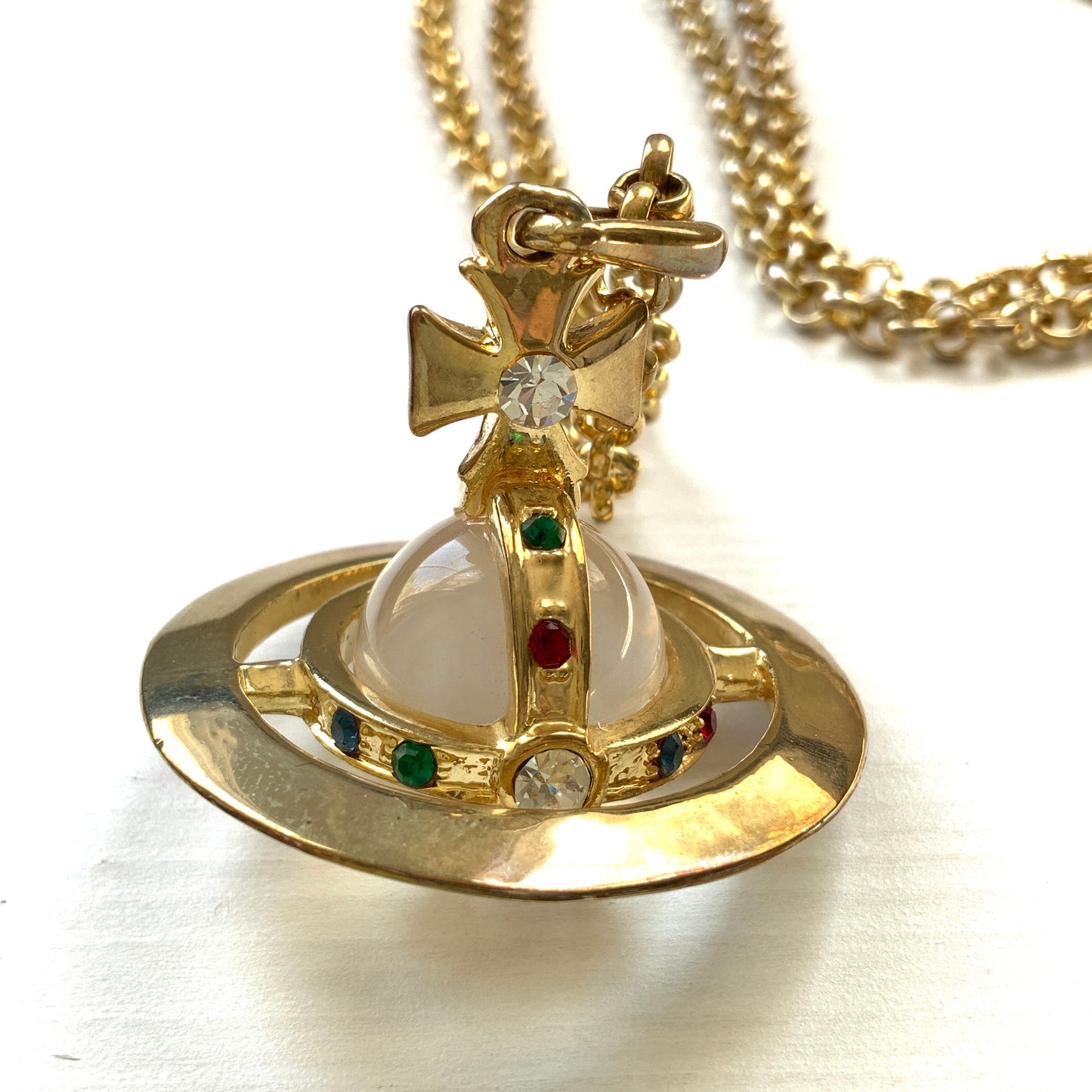 A striking pendant necklace featuring a decorative orb encircled by a metal hoop, resembling the rings of Saturn. カラフルなストーンで飾られた宝珠(キリスト教圏で、十字架をのせた球体として王権の象徴に用いられるモチーフ)を、まるで土星の輪のようなメタルフープで囲んだデザインのペンダントネックレスです。