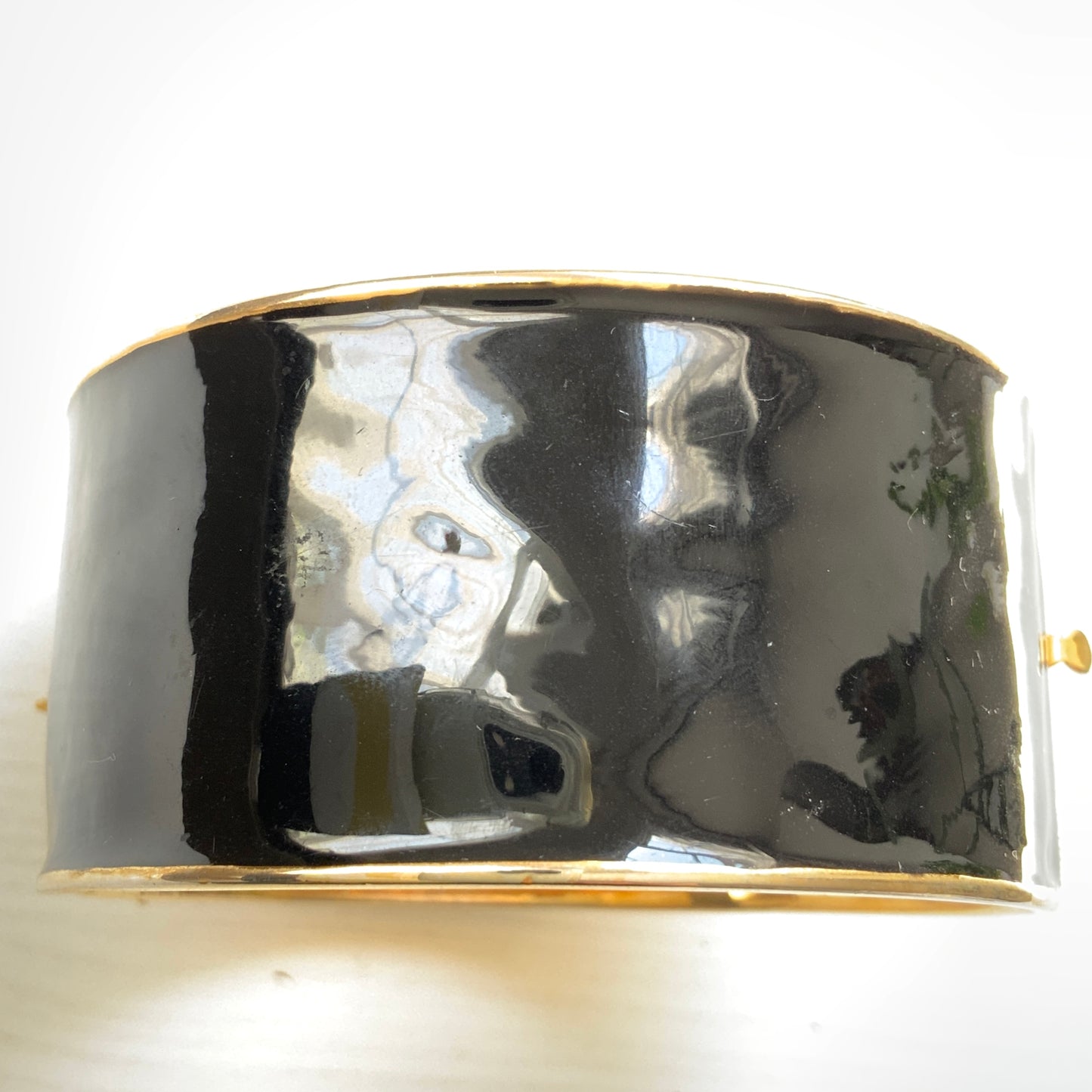 A wide bangle featuring celestial motifs in gold tone set against glossy black enamel. ブラックエナメルに、ゴールドトーンの天体モチーフが輝く幅広バングル。