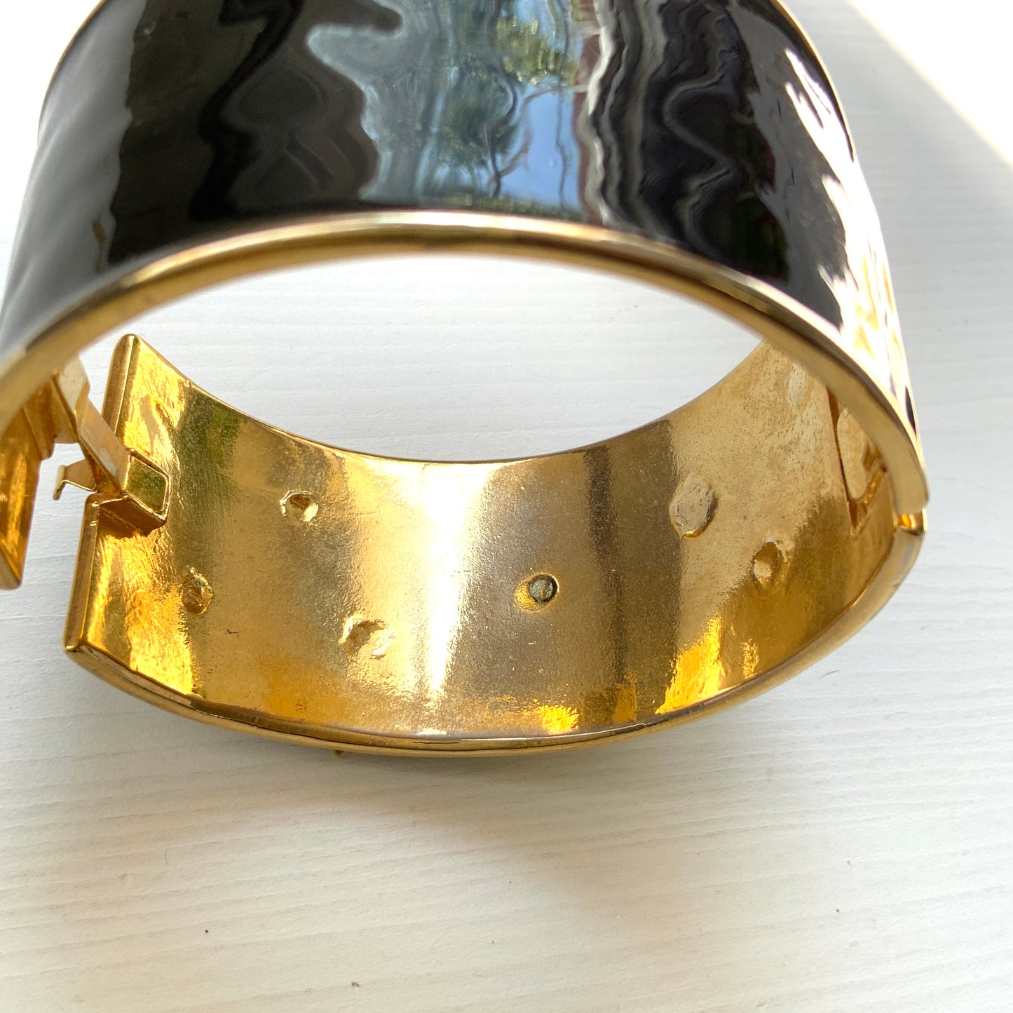 A wide bangle featuring celestial motifs in gold tone set against glossy black enamel. ブラックエナメルに、ゴールドトーンの天体モチーフが輝く幅広バングル。