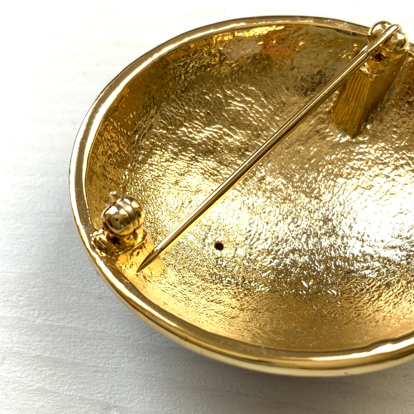 A dome-shaped brooch adorned with vibrant blue enamel, featuring silver-tone celestial motifs such as the sun face, crescent moon face, Saturn, and stars. 鮮やかなブルーのエナメルが施されたドームに、シルバートーンの太陽や三日月フェイスや、土星や星などが浮かんだブローチ。