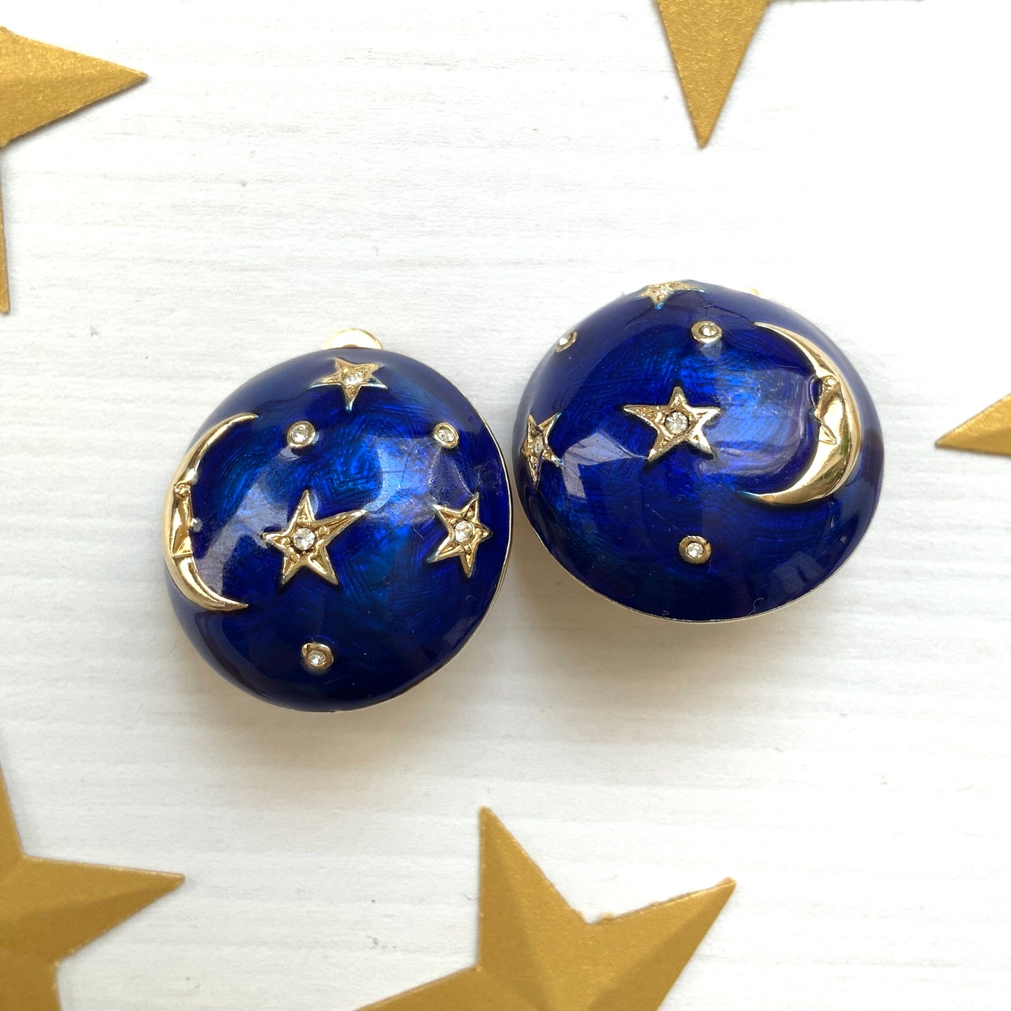 Clip-on earrings featuring a vibrant blue enamel dome, with silver-tone crescent moon faces and stars floating across the surface. 鮮やかなブルーエナメルのドームに、シルバートーンの三日月ムーンフェイスや星が浮かんだクリップイヤリング。