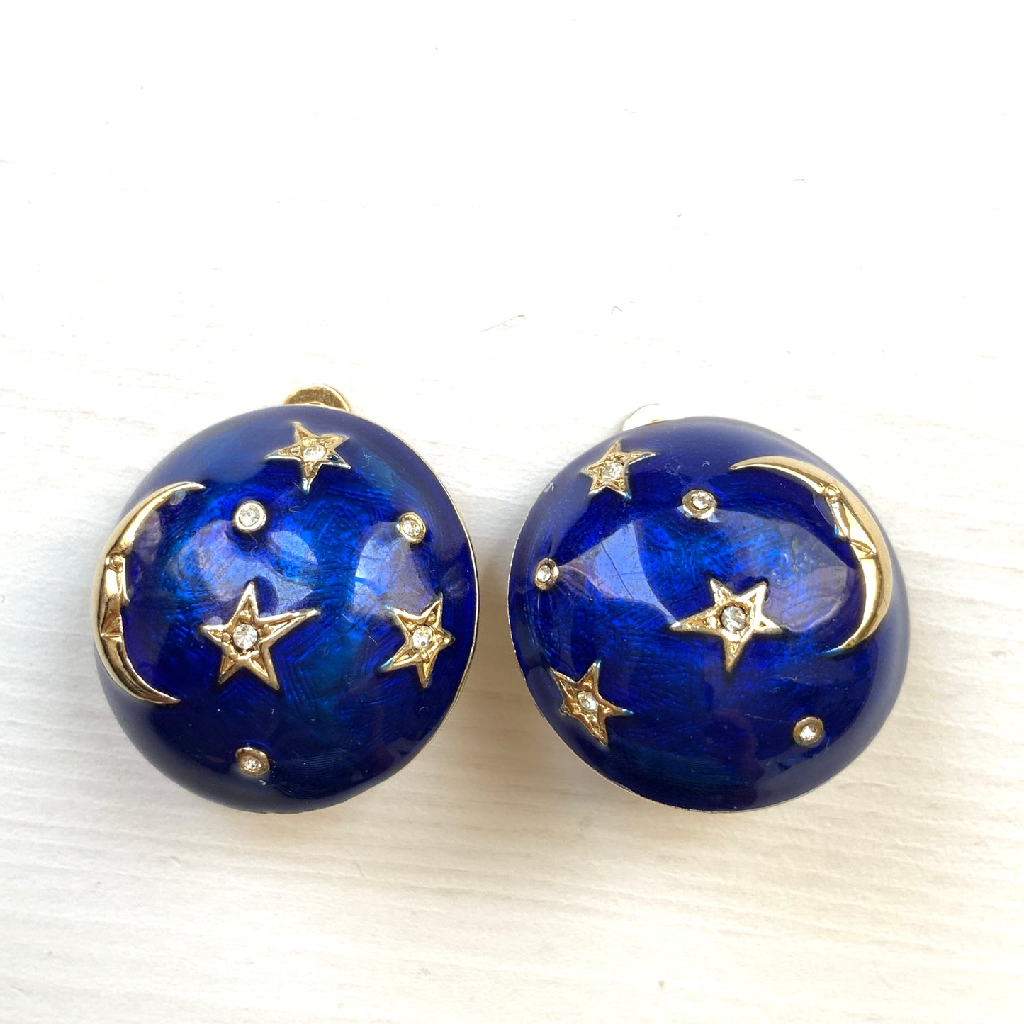 Clip-on earrings featuring a vibrant blue enamel dome, with silver-tone crescent moon faces and stars floating across the surface. 鮮やかなブルーエナメルのドームに、シルバートーンの三日月ムーンフェイスや星が浮かんだクリップイヤリング。
