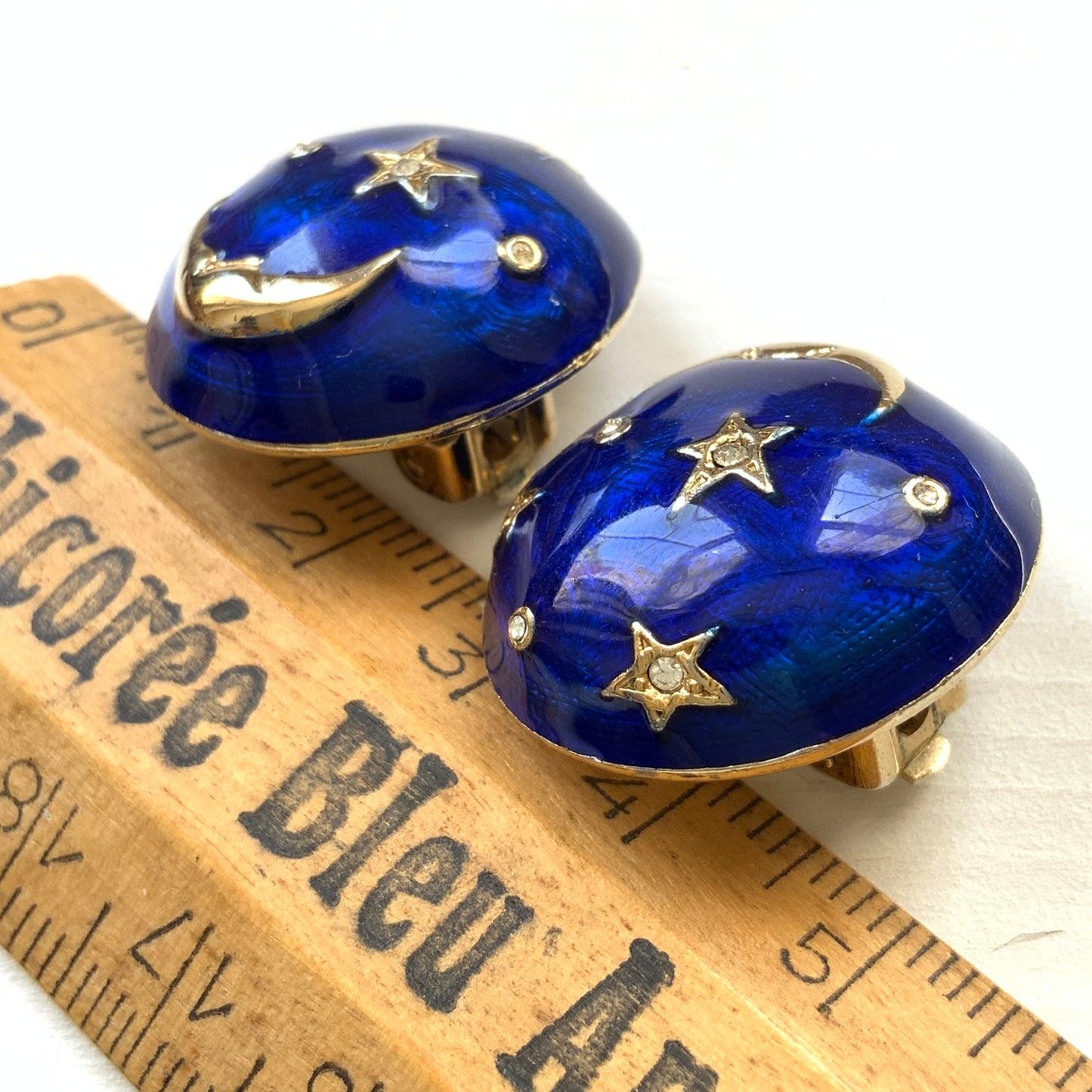 Clip-on earrings featuring a vibrant blue enamel dome, with silver-tone crescent moon faces and stars floating across the surface. 鮮やかなブルーエナメルのドームに、シルバートーンの三日月ムーンフェイスや星が浮かんだクリップイヤリング。