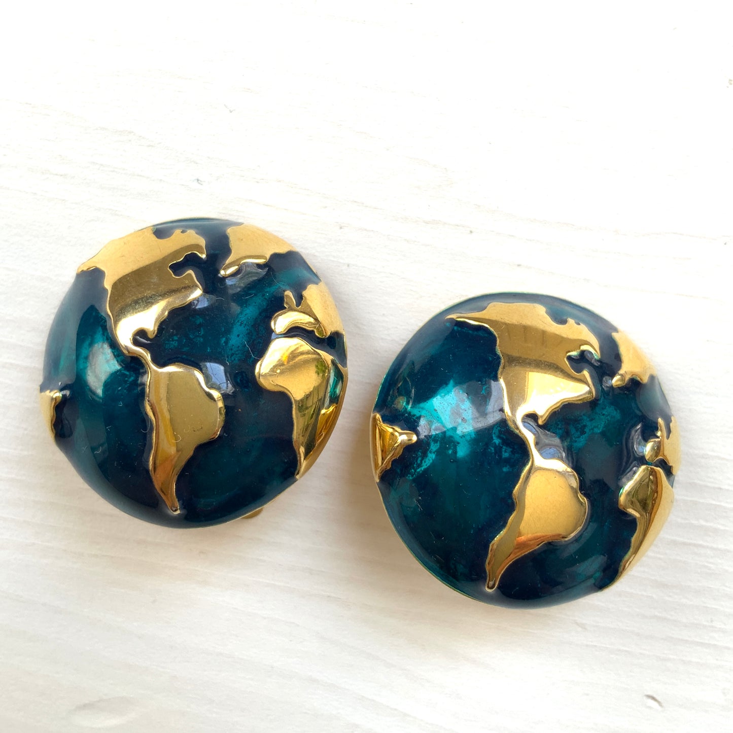 Clip-on earrings featuring a globe design with gold tone continents over a dome of deep ocean blue enamel. 深い海の色のエナメルドームにゴールドトーンで大陸をあしらった地球のクリップイヤリング。