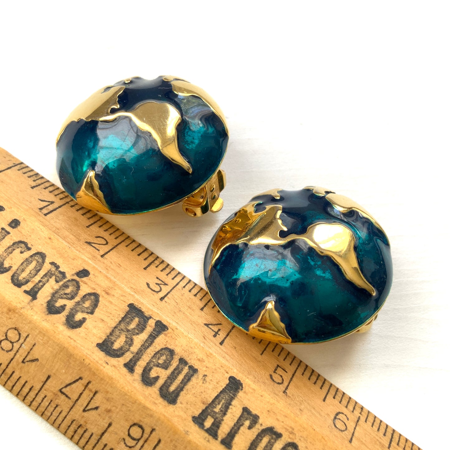 Clip-on earrings featuring a globe design with gold tone continents over a dome of deep ocean blue enamel. 深い海の色のエナメルドームにゴールドトーンで大陸をあしらった地球のクリップイヤリング。