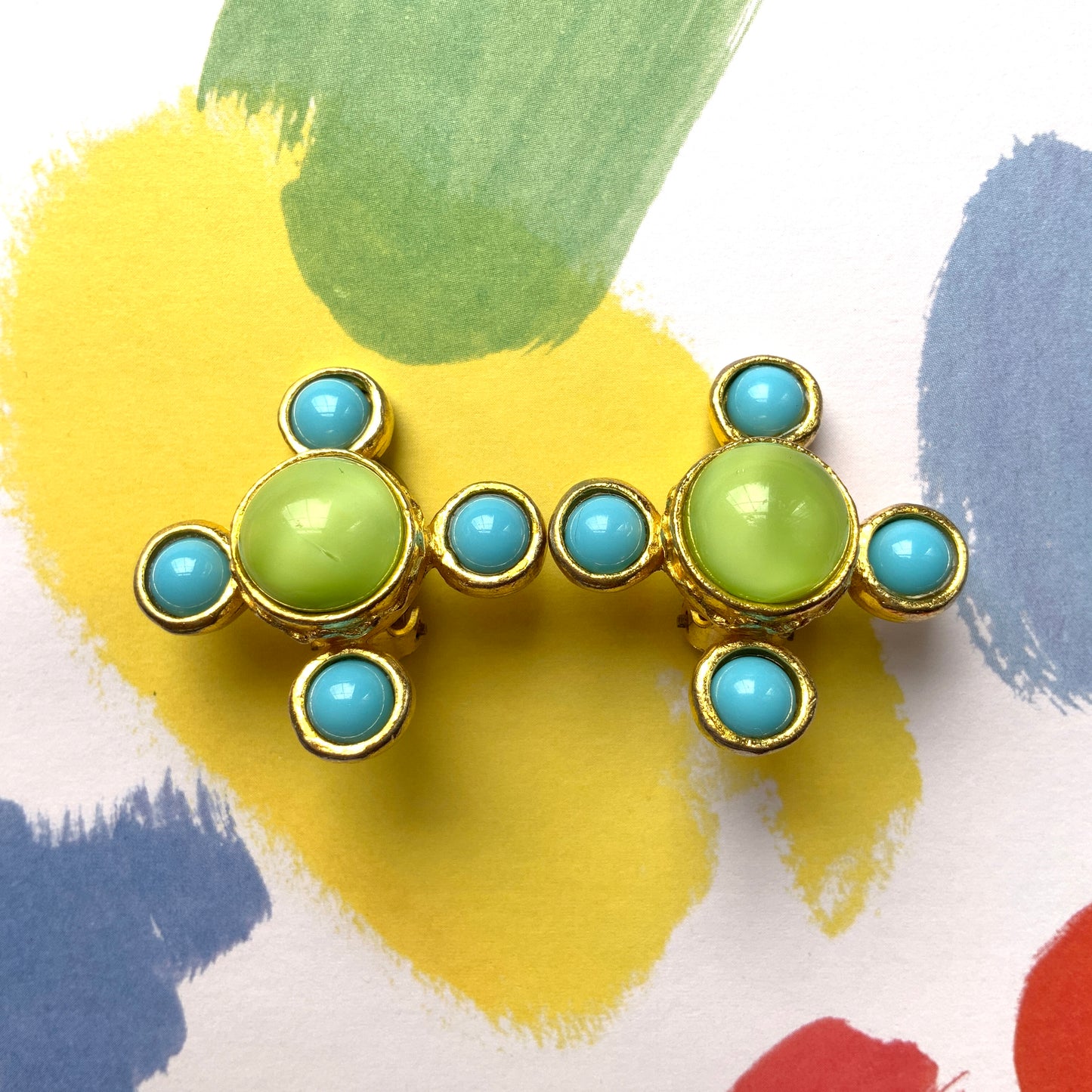 These clip-on earrings by Farah Lister feature a striking cross design with a refreshing apple green satin cabochon glass at the centre, paired with vivid turquoise glass stones. 爽やかなアップルグリーンのサテンカボショングラスとヴィヴィッドなターコイズグラスがクロスになった、ファラー・リスターのクリップイヤリング。