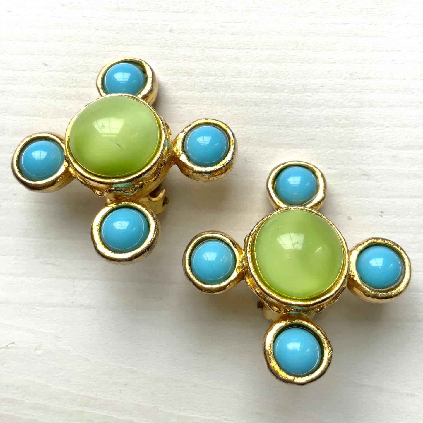 These clip-on earrings by Farah Lister feature a striking cross design with a refreshing apple green satin cabochon glass at the centre, paired with vivid turquoise glass stones. 爽やかなアップルグリーンのサテンカボショングラスとヴィヴィッドなターコイズグラスがクロスになった、ファラー・リスターのクリップイヤリング。