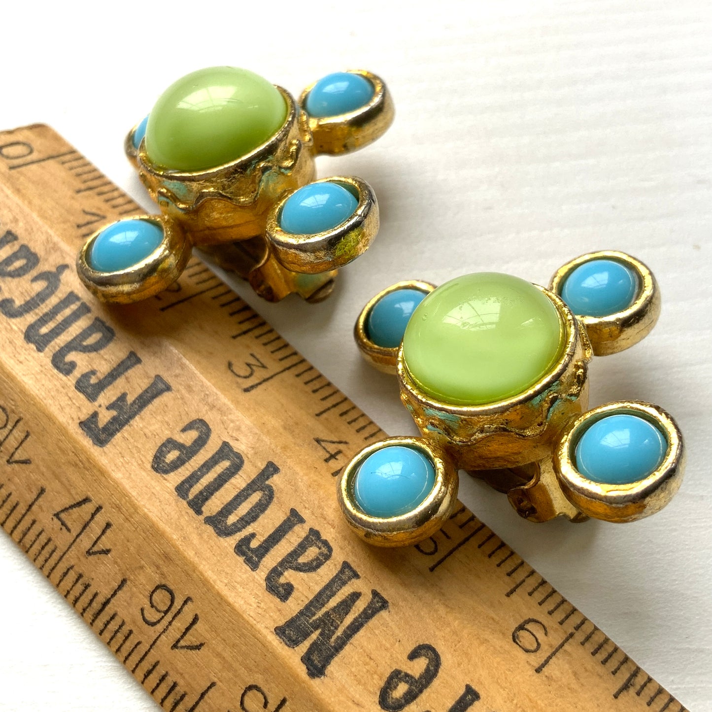 These clip-on earrings by Farah Lister feature a striking cross design with a refreshing apple green satin cabochon glass at the centre, paired with vivid turquoise glass stones. 爽やかなアップルグリーンのサテンカボショングラスとヴィヴィッドなターコイズグラスがクロスになった、ファラー・リスターのクリップイヤリング。
