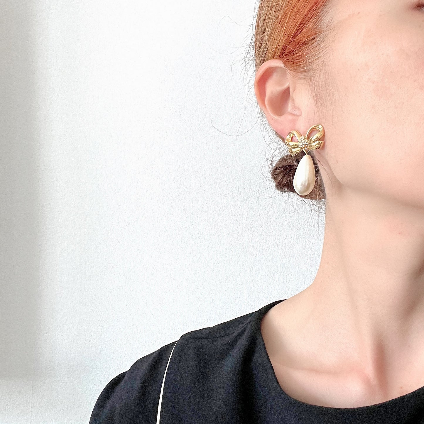 A pair of clip-on earrings featuring a bow motif in gold-tone metal, with large teardrop-shaped faux pearls that sway beautifully as you move. ゴールドトーンメタルのリボンモチーフに、大ぶりのティアドロップ型フォーパールが揺れるクリップイヤリング。