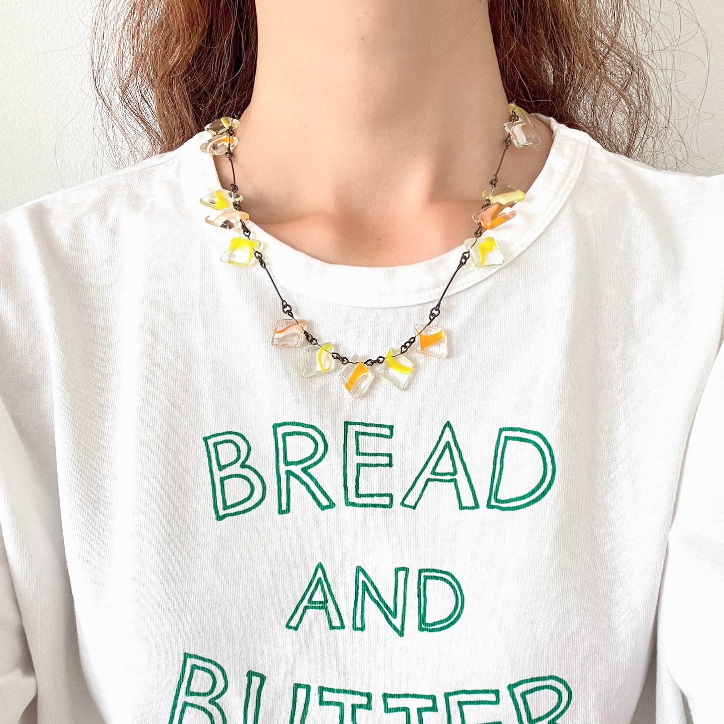 Necklace featuring diamond-shaped clear glass beads infused with shades of yellow, orange, and white. クリアのダイヤ型グラスにイエロー、オレンジ、ホワイトのカラーが入ったビーズを使ったネックレス。