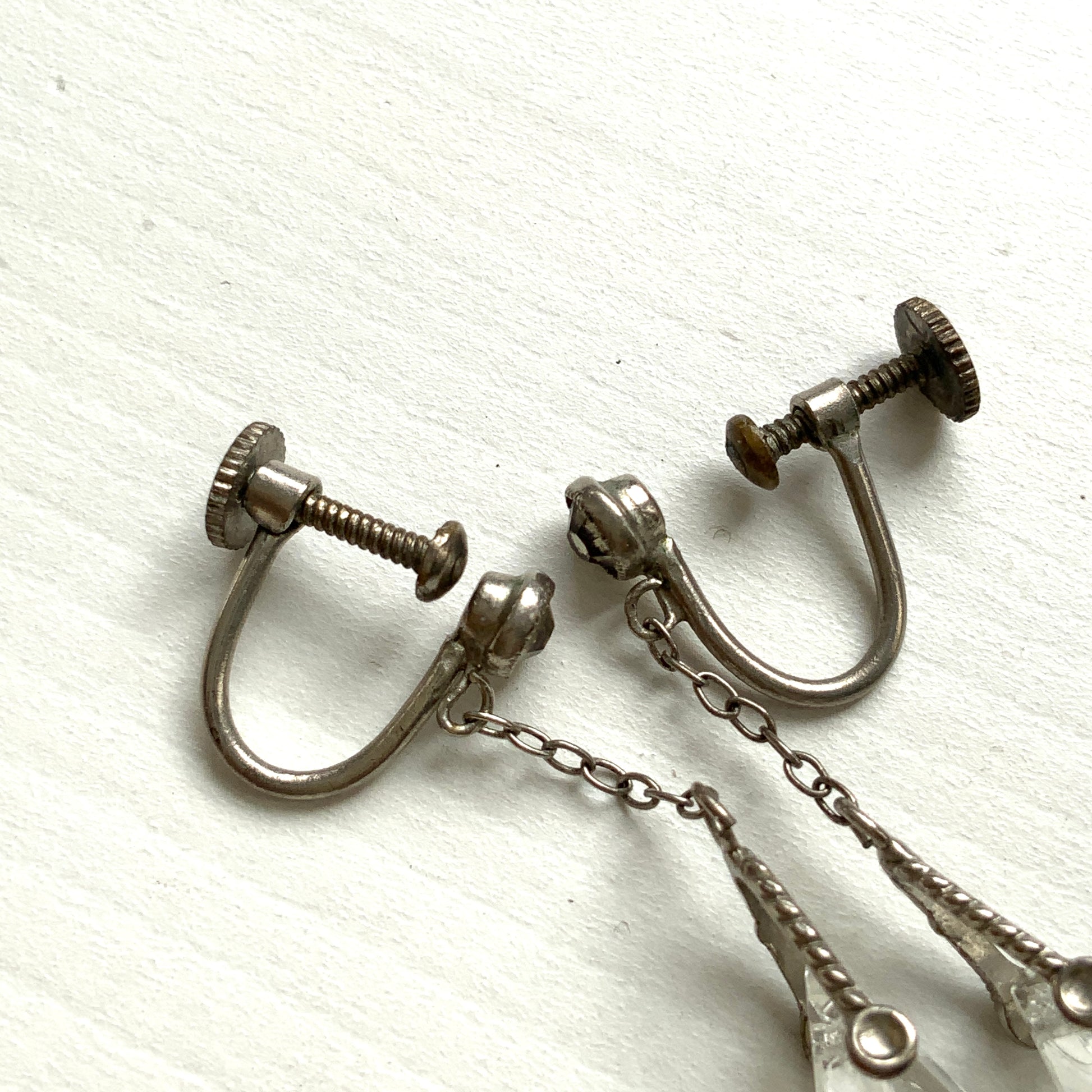 Screw-back earrings featuring clear faceted glass in a unique triangular form. ユニークな三角フォルムのファセットグラスが揺れる、スクリューイヤリング。