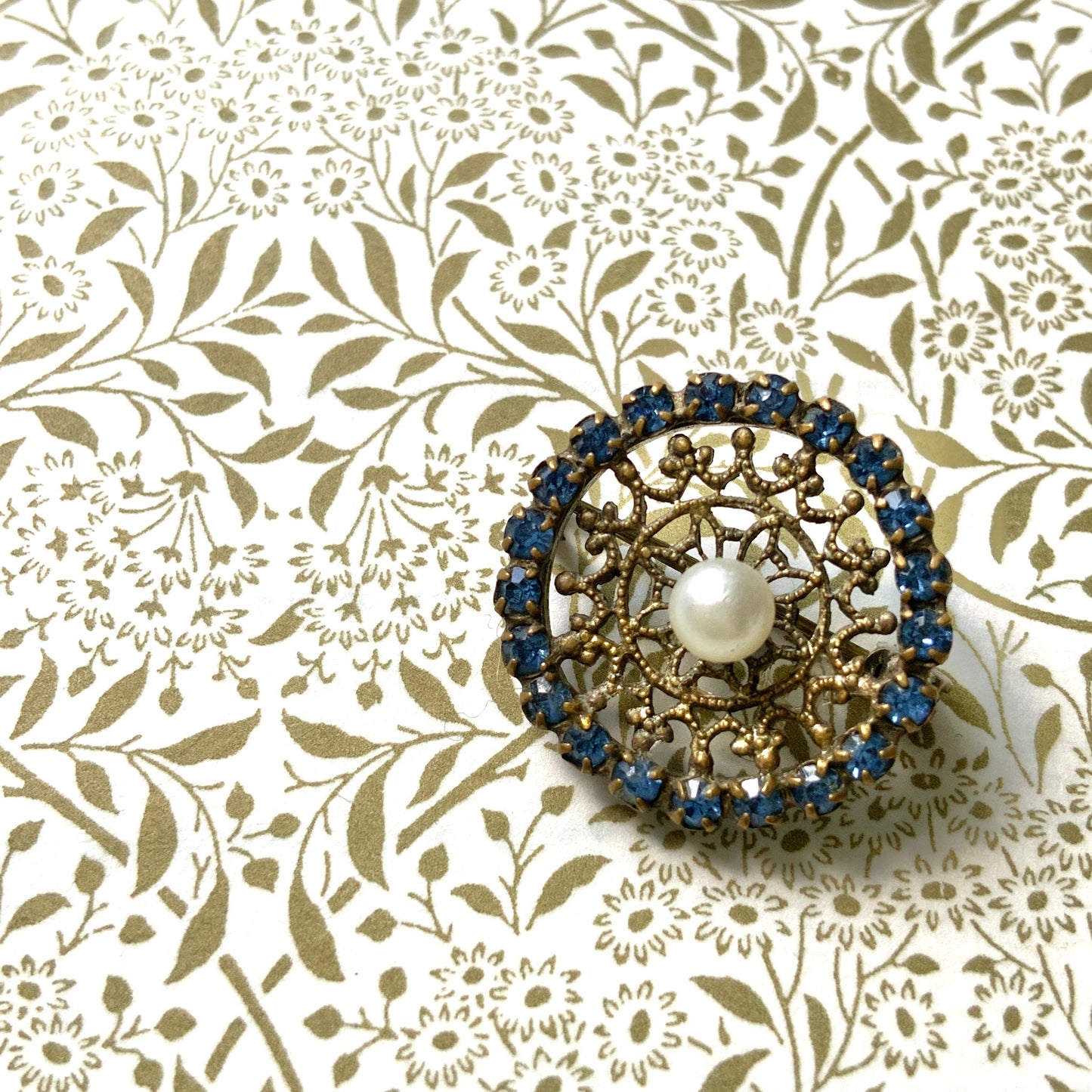 This petite brooch features a delicate round gold-tone filigree, crowned with a small glass pearl. 繊細なラウンドのゴールドトーン フィリグリーに、グラスパールがちょこんと乗ったミニブローチ。