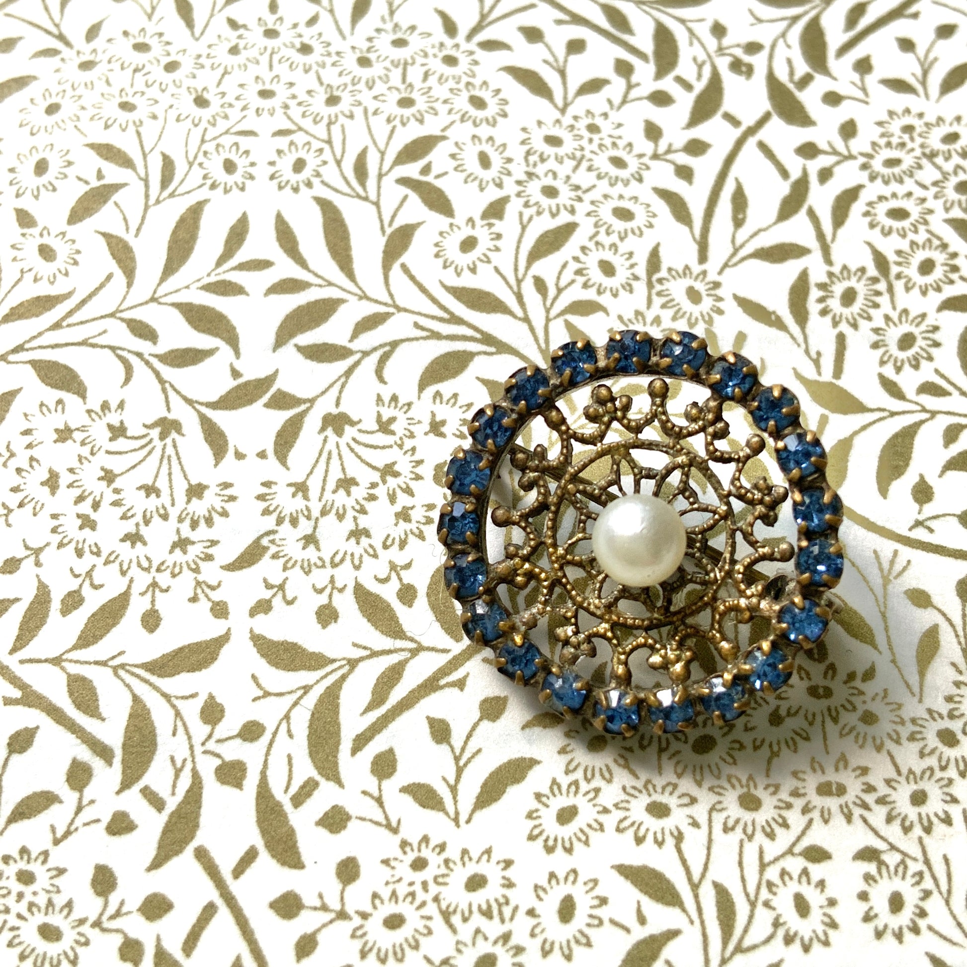 This petite brooch features a delicate round gold-tone filigree, crowned with a small glass pearl. 繊細なラウンドのゴールドトーン フィリグリーに、グラスパールがちょこんと乗ったミニブローチ。