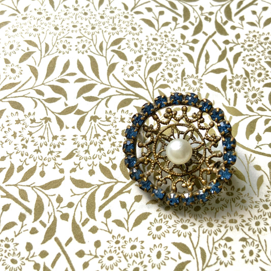 This petite brooch features a delicate round gold-tone filigree, crowned with a small glass pearl. 繊細なラウンドのゴールドトーン フィリグリーに、グラスパールがちょこんと乗ったミニブローチ。